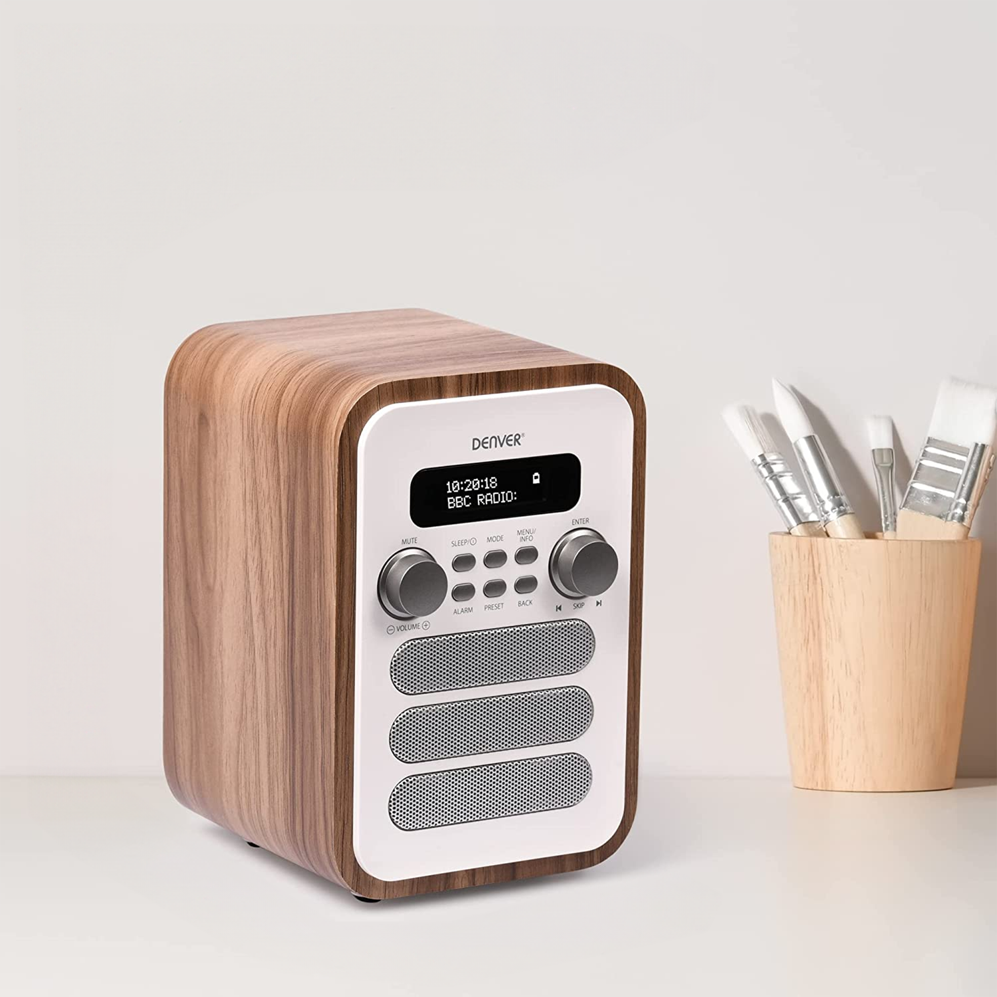Drewniane radio z wyświetlaczem cyfrowym i przyciskami stoi na białej powierzchni, z pędzlami w tle.