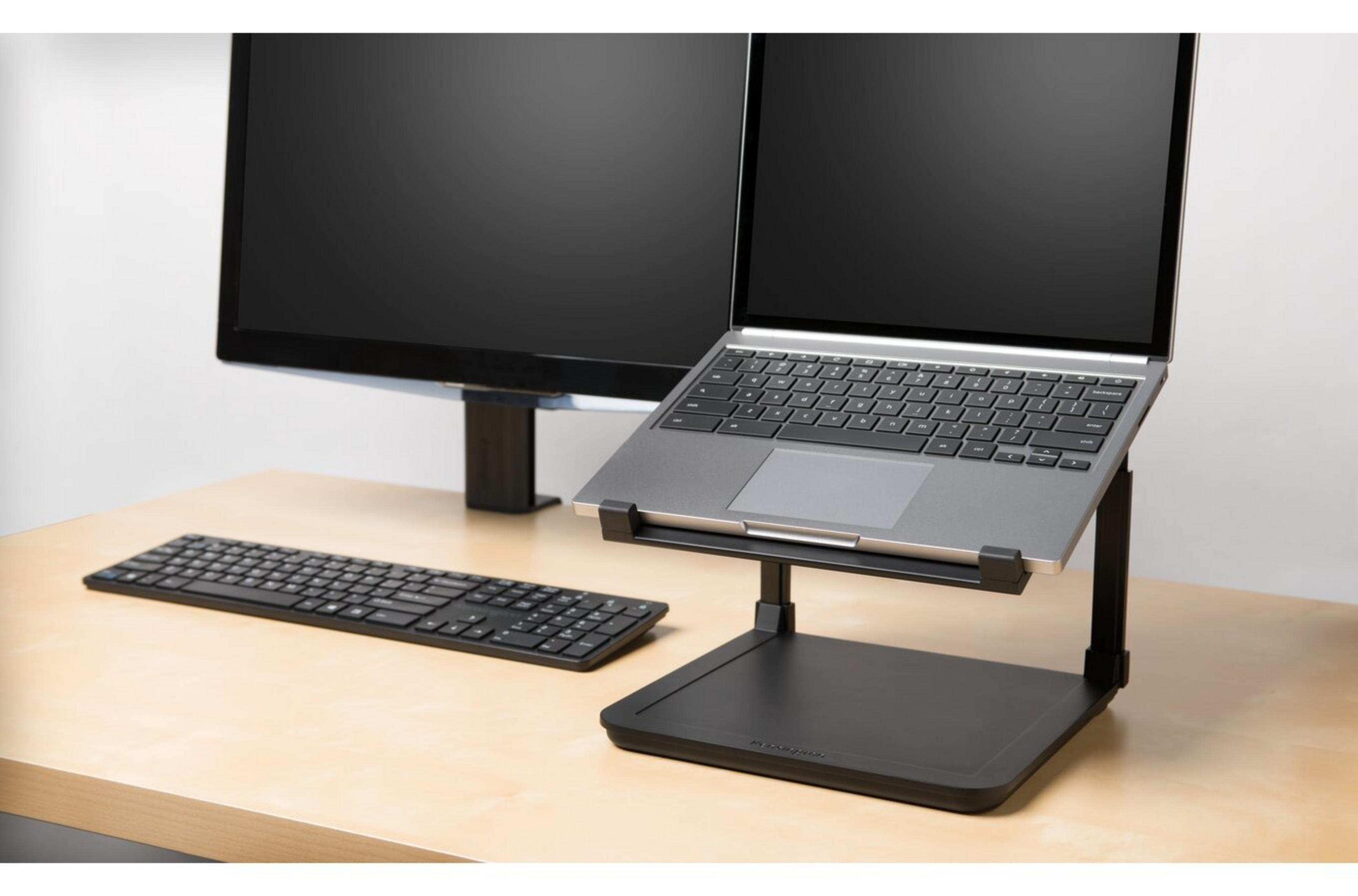 Laptop auf einem Ständer, Tastatur und Monitor auf einem hellen Holzschreibtisch.