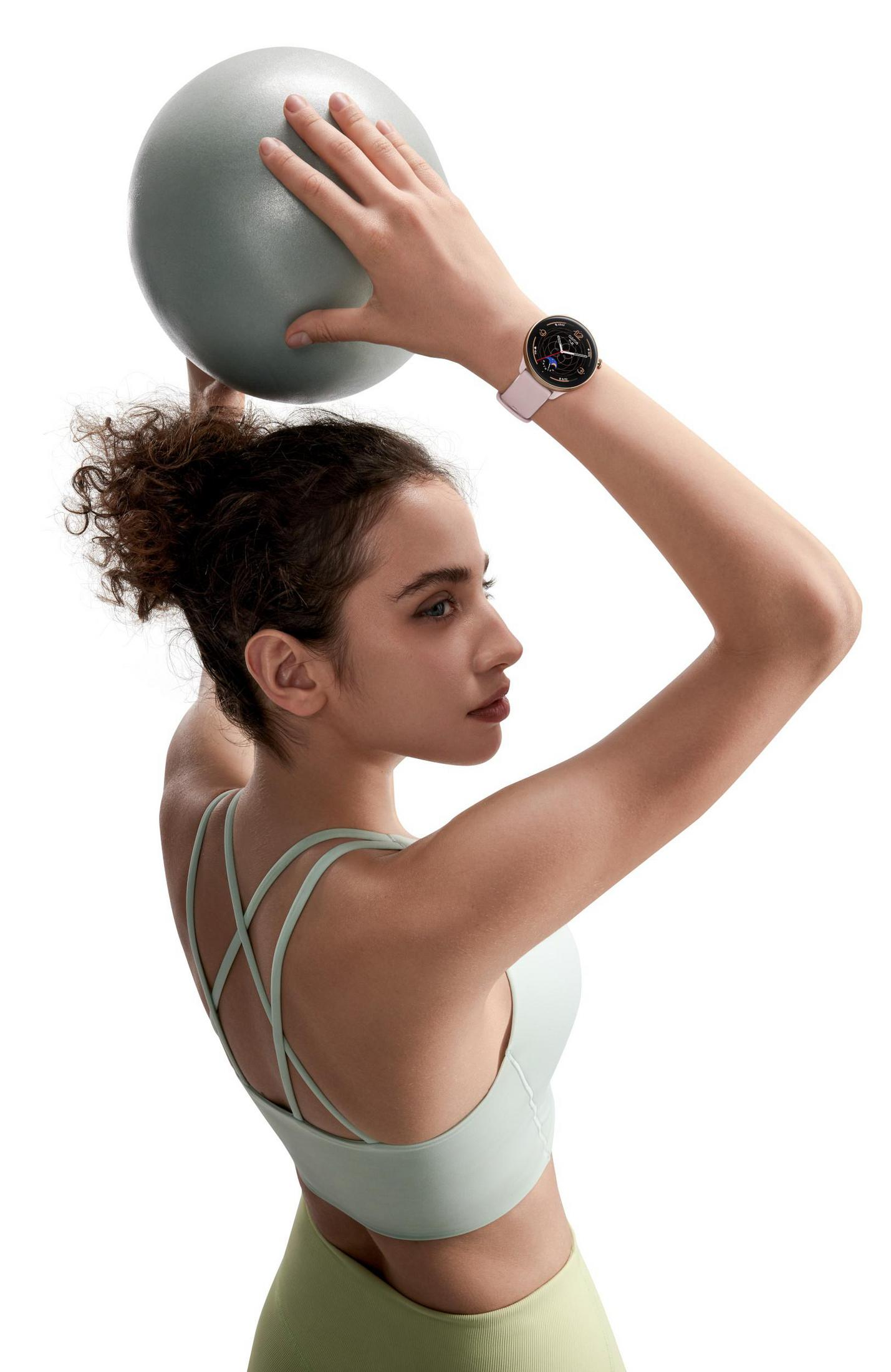 Donna in palestra che tiene una palla con uno smartwatch al polso.