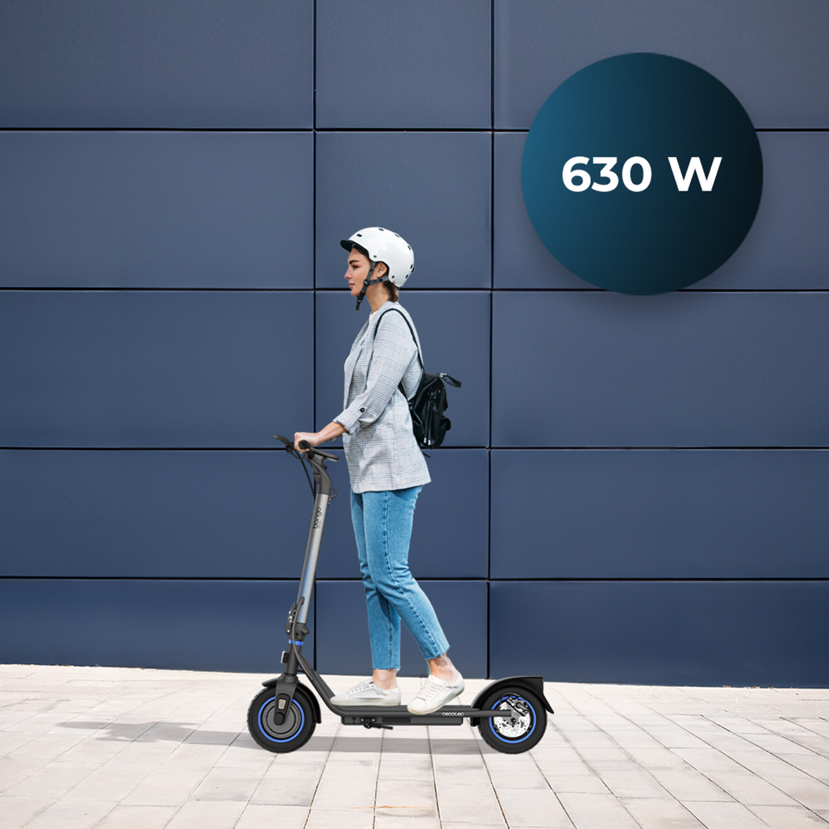 Mujer montando un patinete eléctrico azul y plateado en una acera, potencia de 630W mostrada.