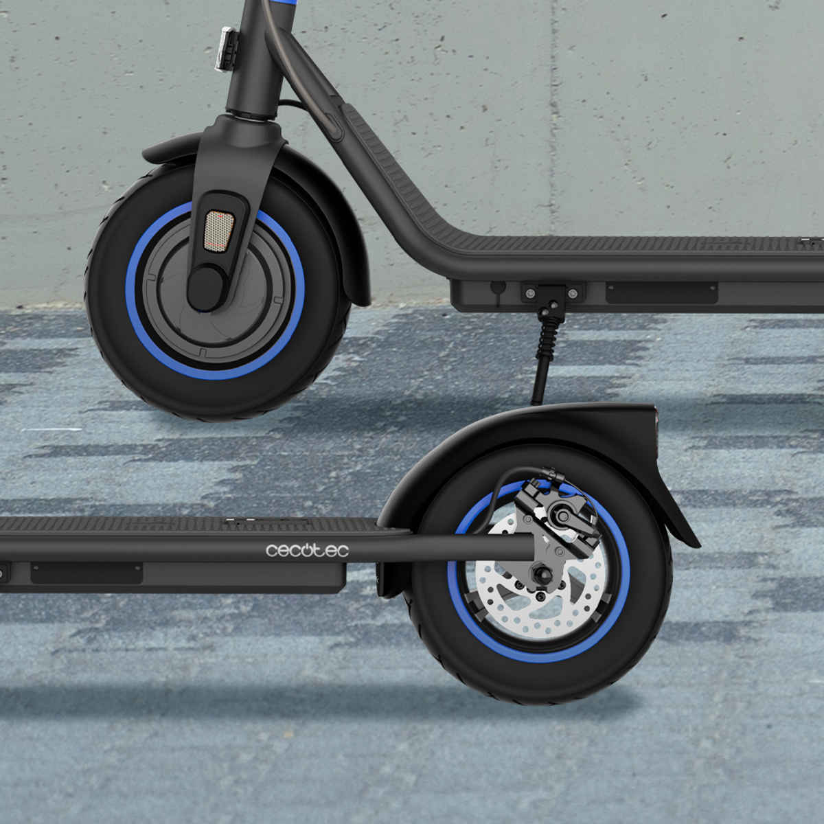 Patinete eléctrico negro y azul con dos ruedas. El patinete está sobre una superficie gris. Detalles de las ruedas visibles.