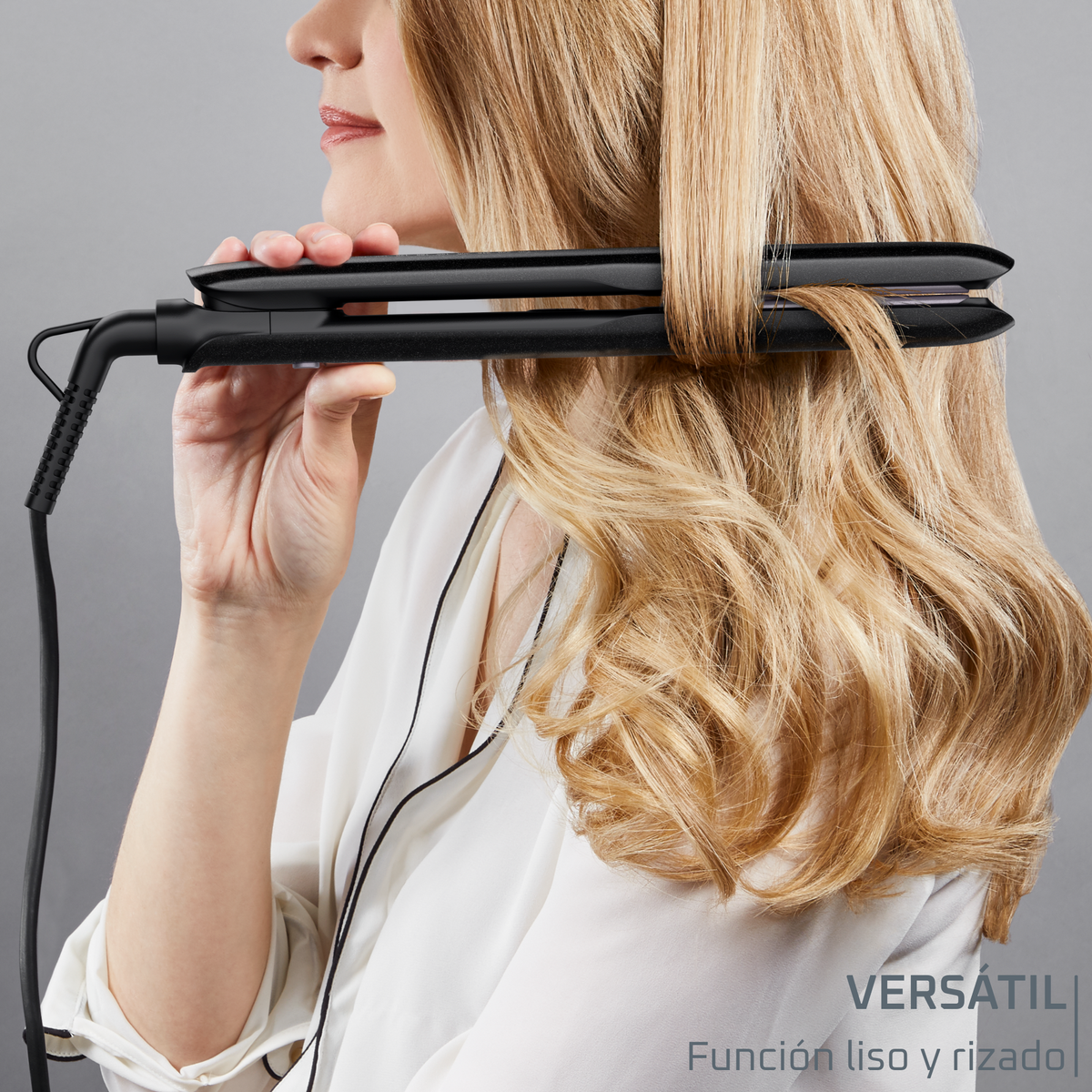 A woman using a black hair straightener on blonde hair.