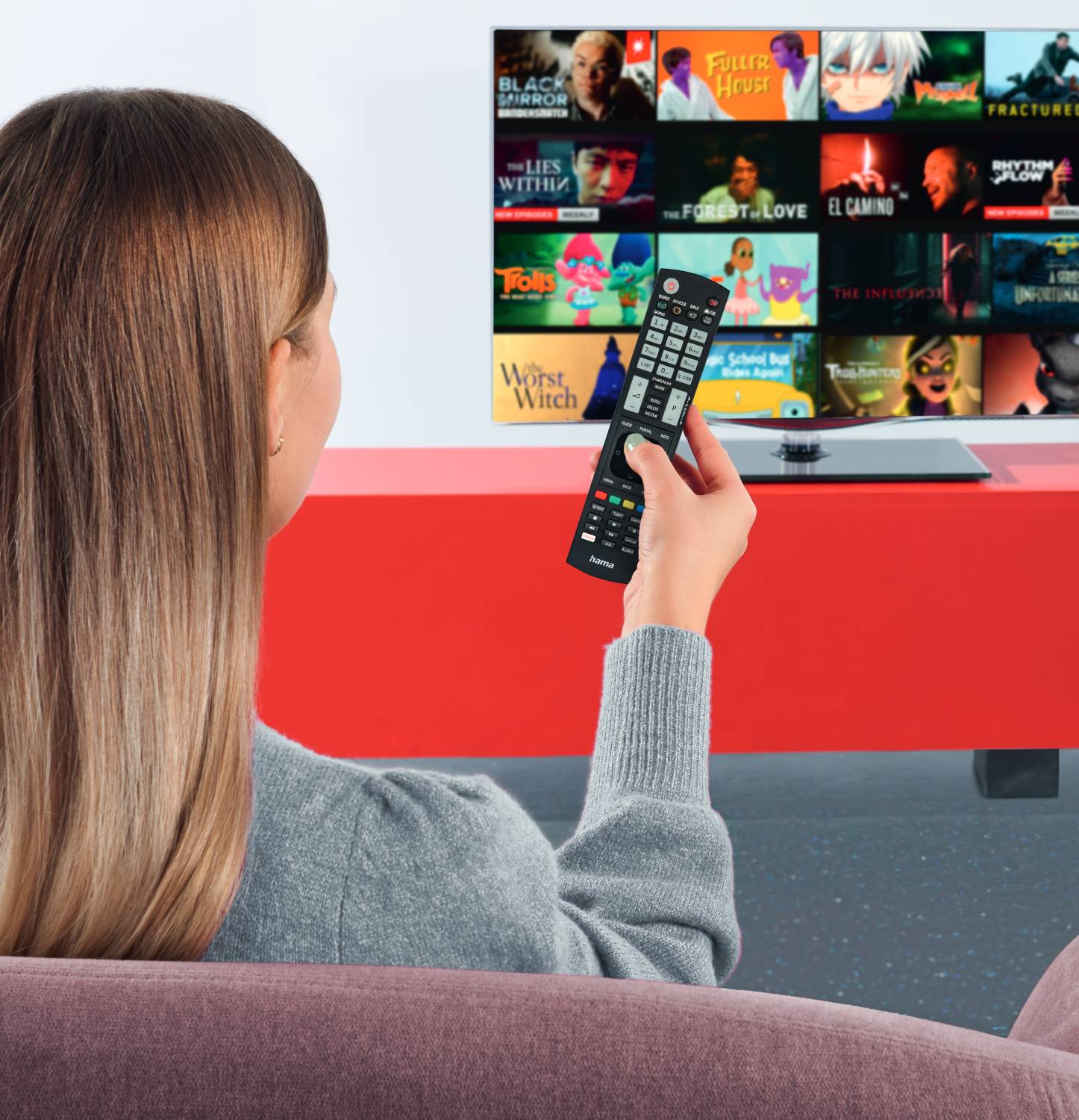 Een vrouw kijkt tv en houdt een afstandsbediening vast. De tv toont filmtitels.