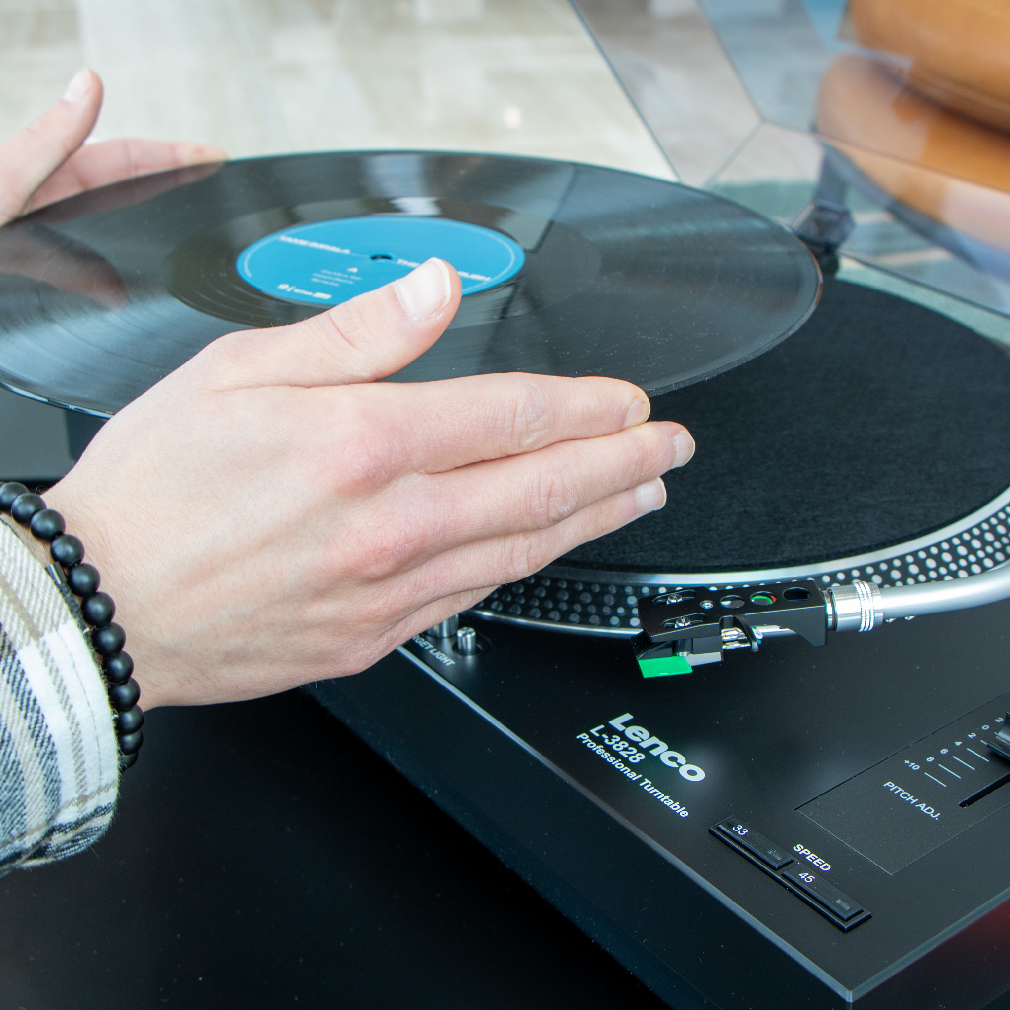 Handen plaatsen een vinylplaat op een zwarte platenspeler.
