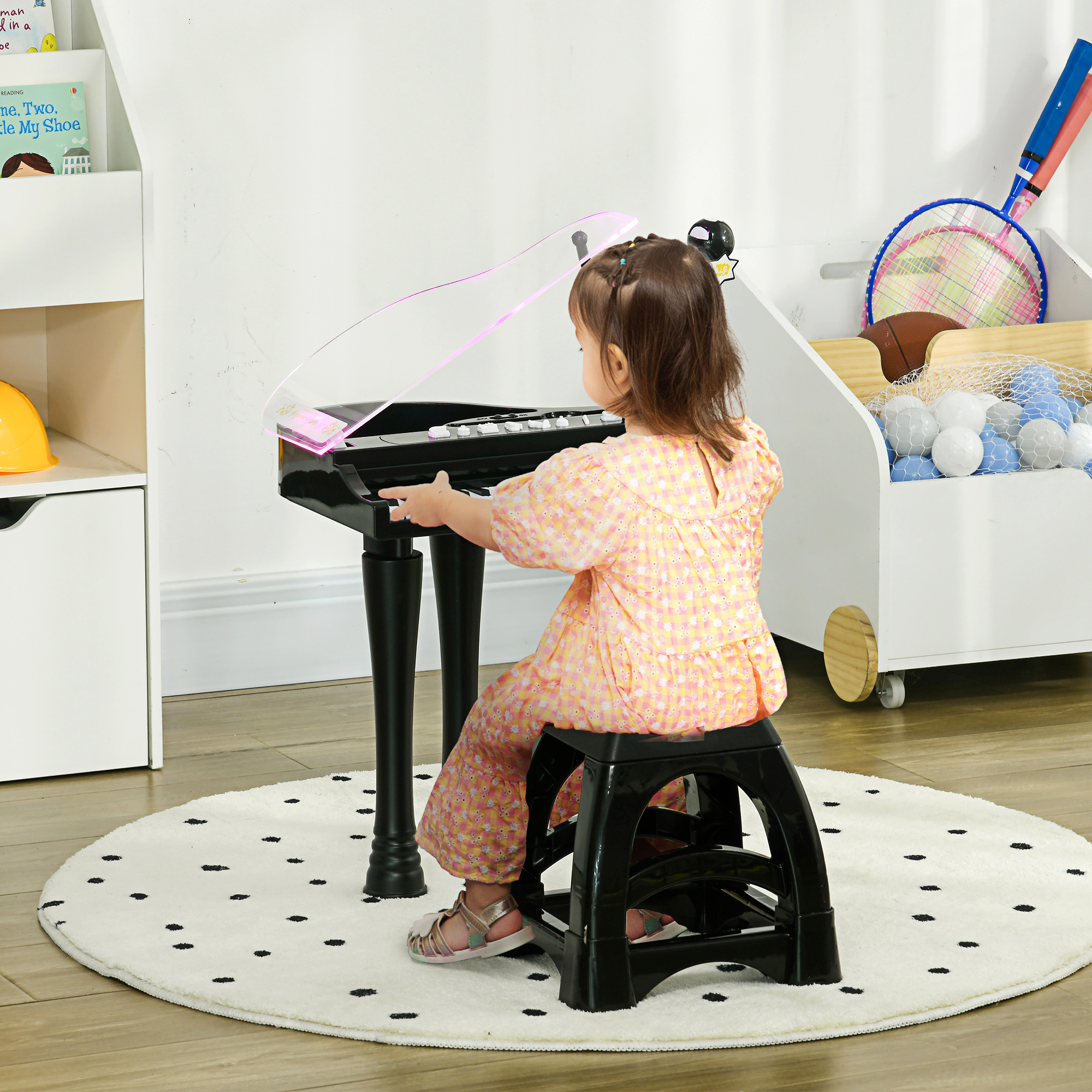 Una niña tocando un piano negro. Está sentada en un taburete negro en una habitación con juguetes.