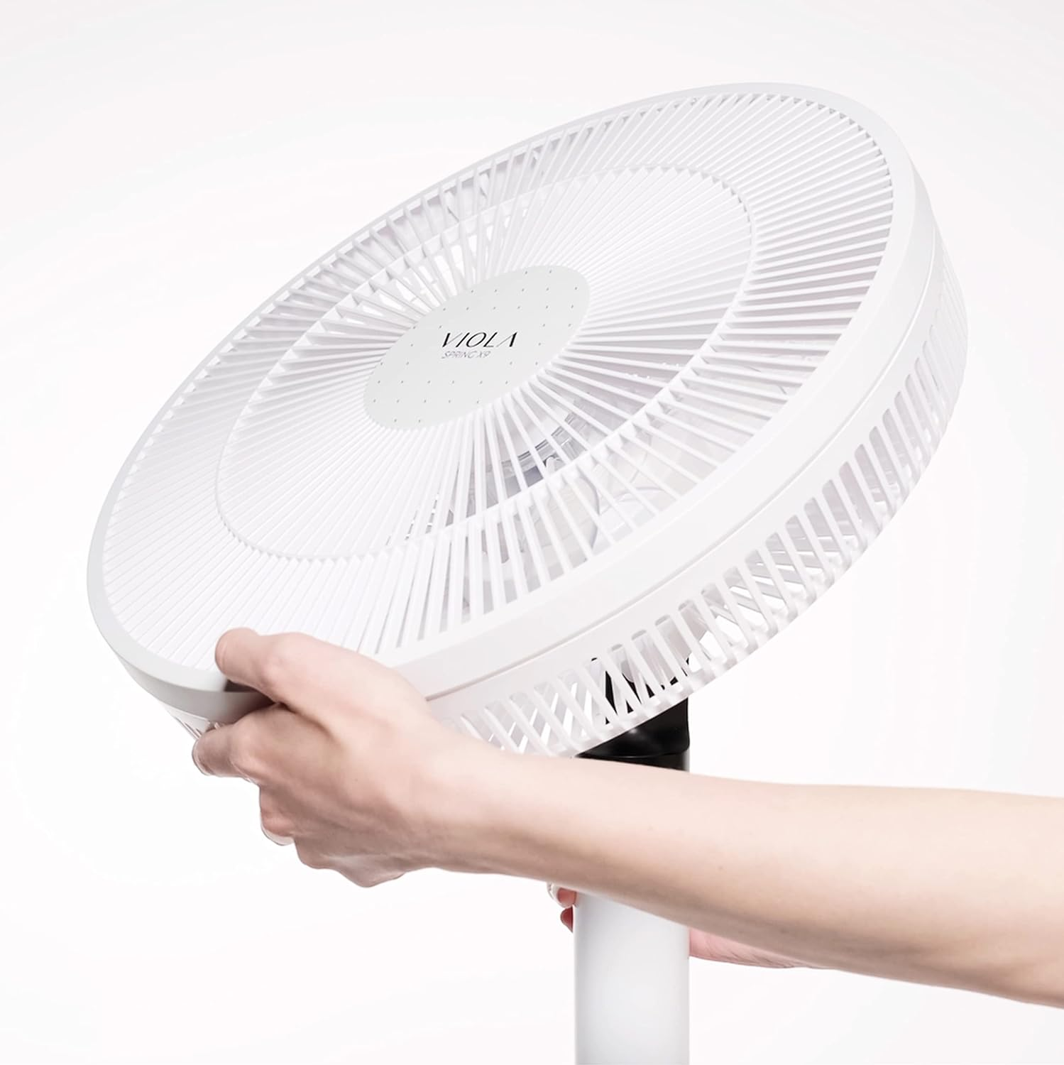 Ventilador blanco sostenido por una mano, en ángulo. Fondo blanco.