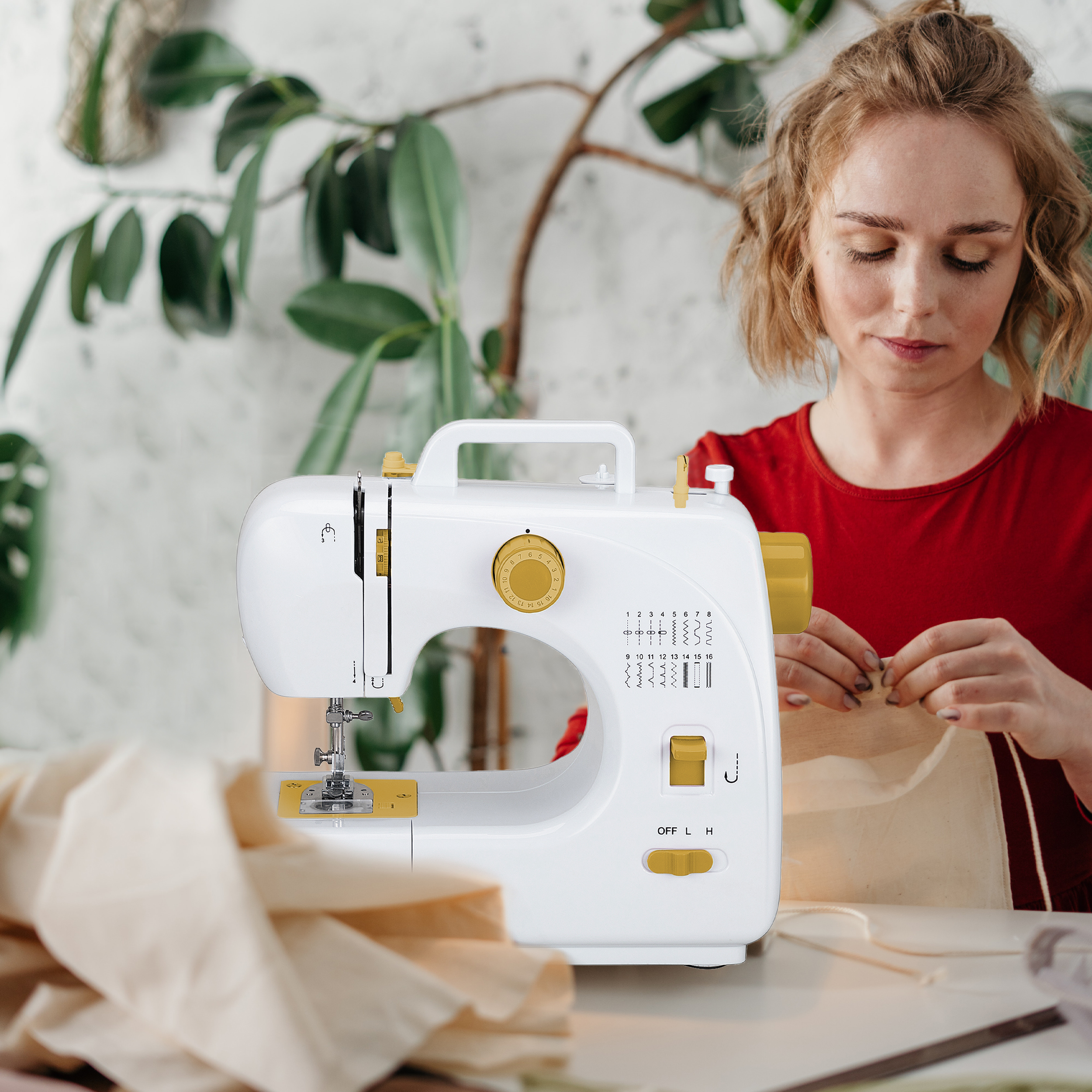 Kobieta szyjąca na białej maszynie do szycia na stole. Beżowa tkanina i akcesoria do szycia w pobliżu.