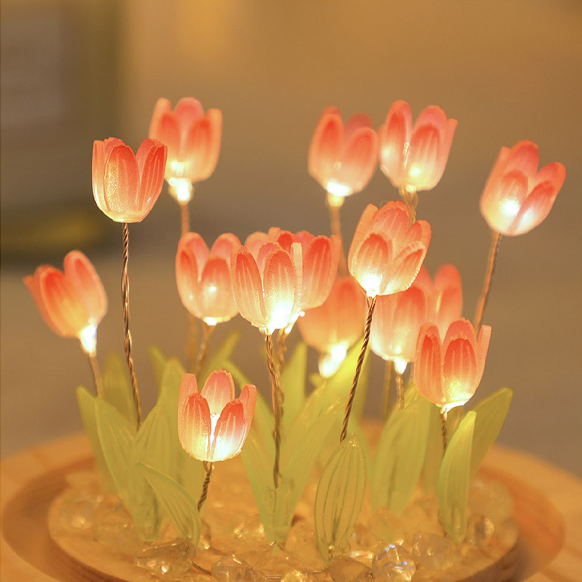Beleuchtete, künstliche Tulpen in einer Glaskuppel. Rosa Blütenblätter, grüne Stiele und leuchtende Lichter. Dunkler Hintergrund.