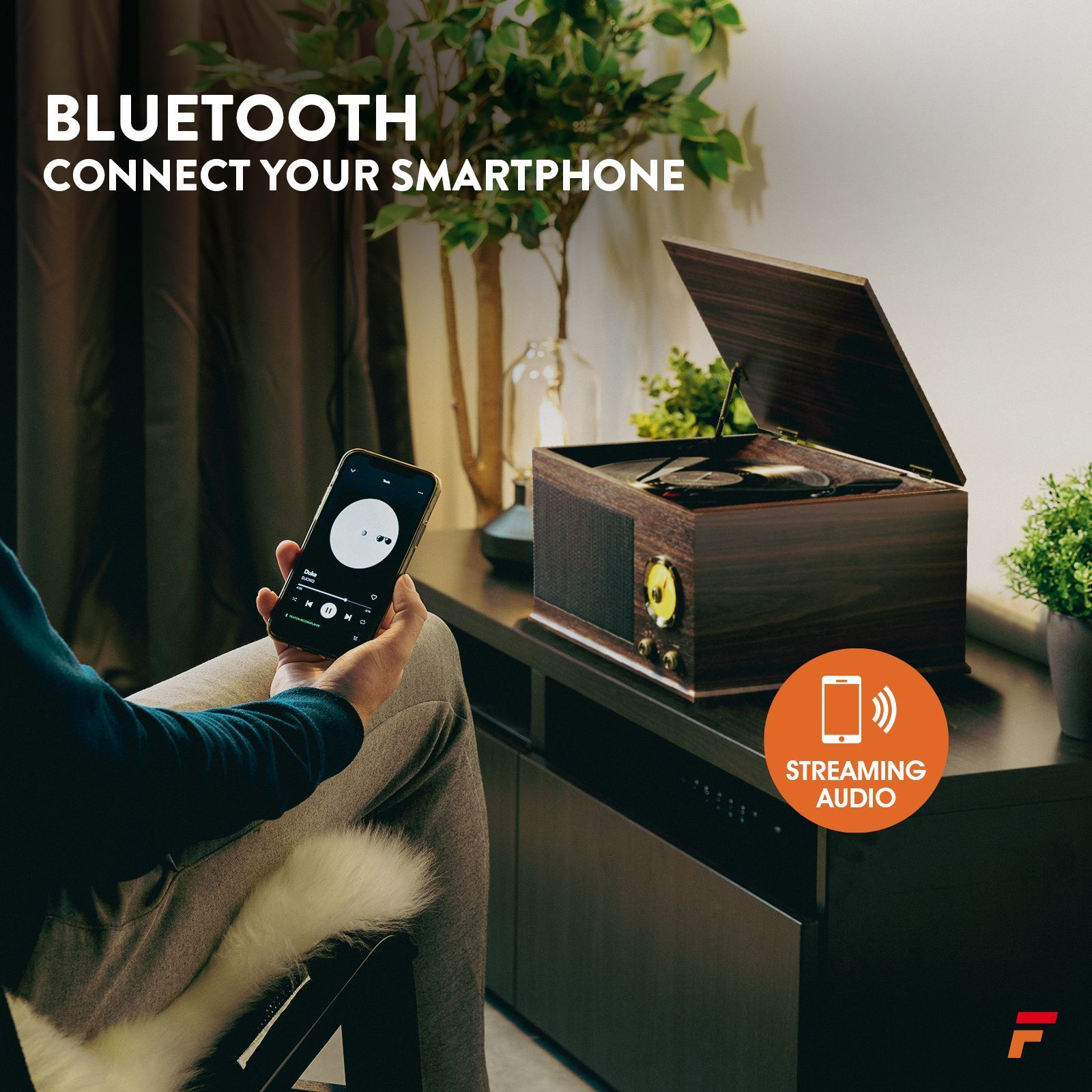 Personne tenant un smartphone à côté d'un lecteur audio en bois. Icône de diffusion audio.