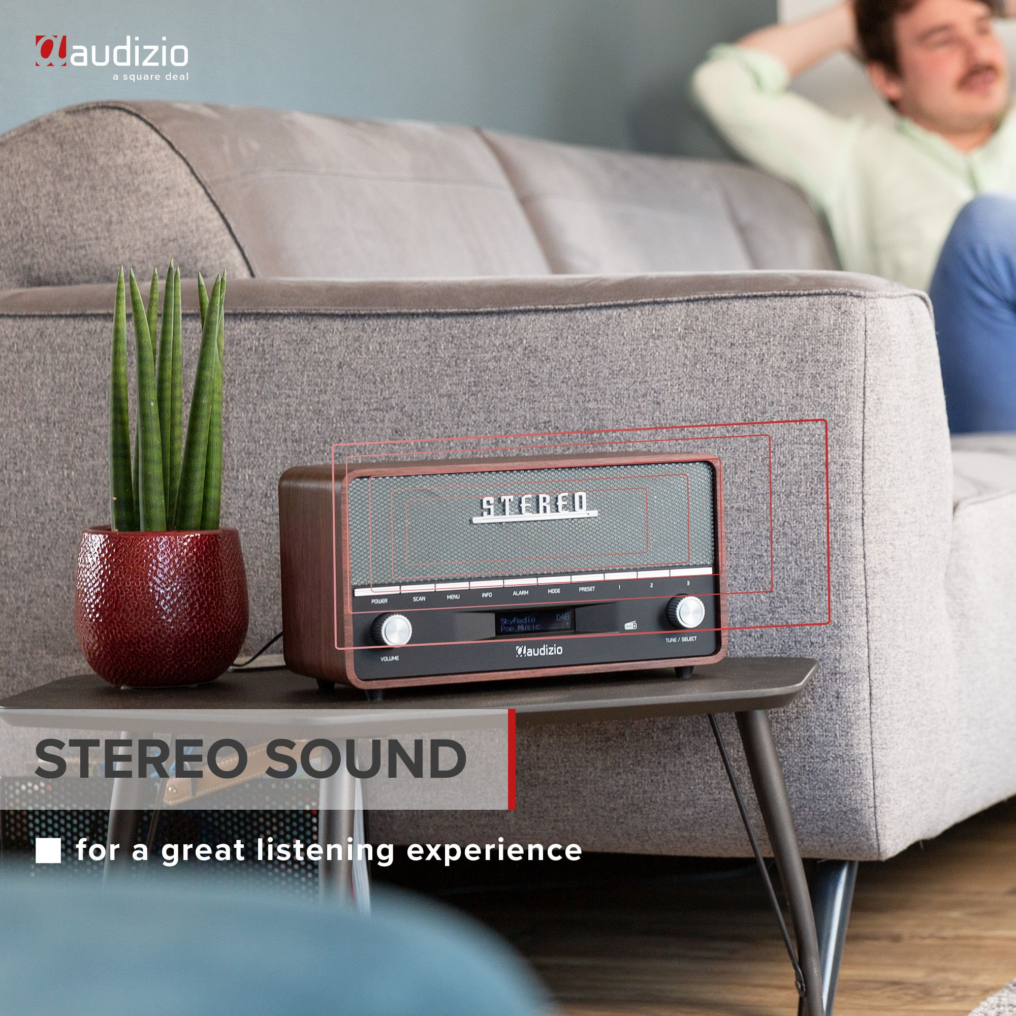 Ein Retro-Stereo-Radio auf einem Tisch neben einer Pflanze und einer Couch.