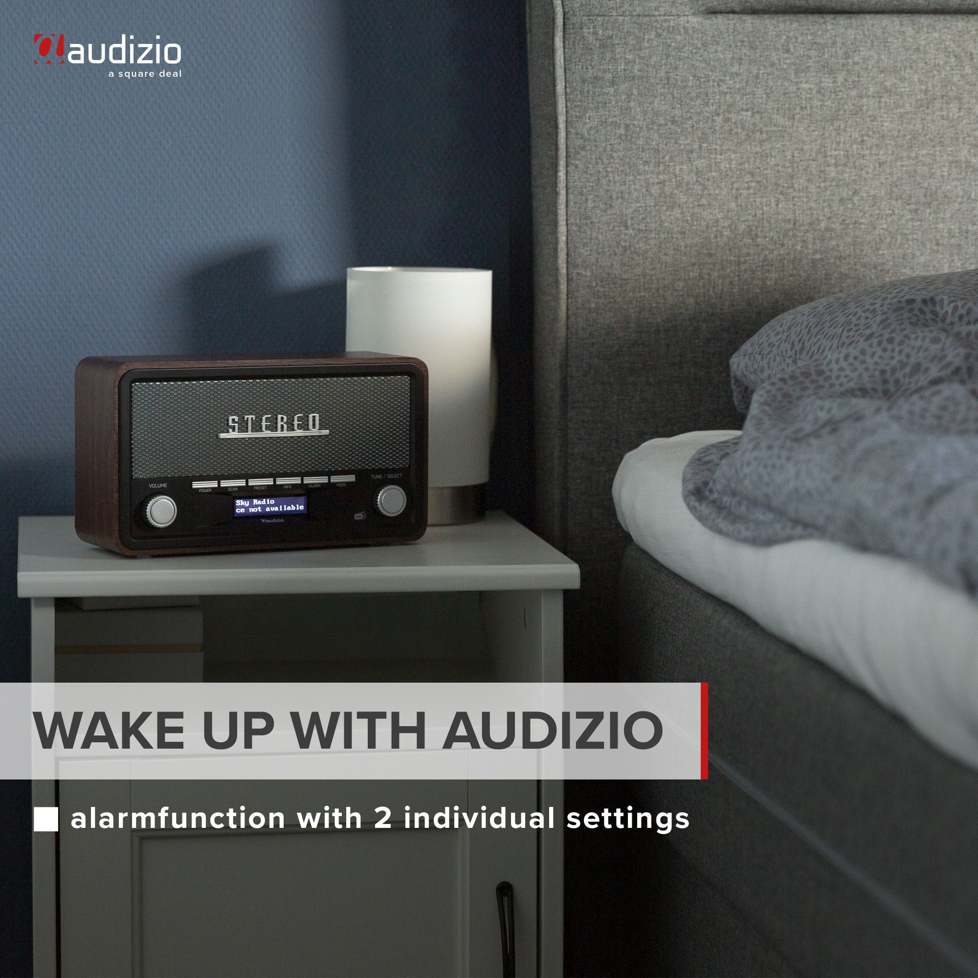 Radio en una mesita de noche, con texto: Wake up with Audizio. Función de alarma. Madera oscura, cama gris.