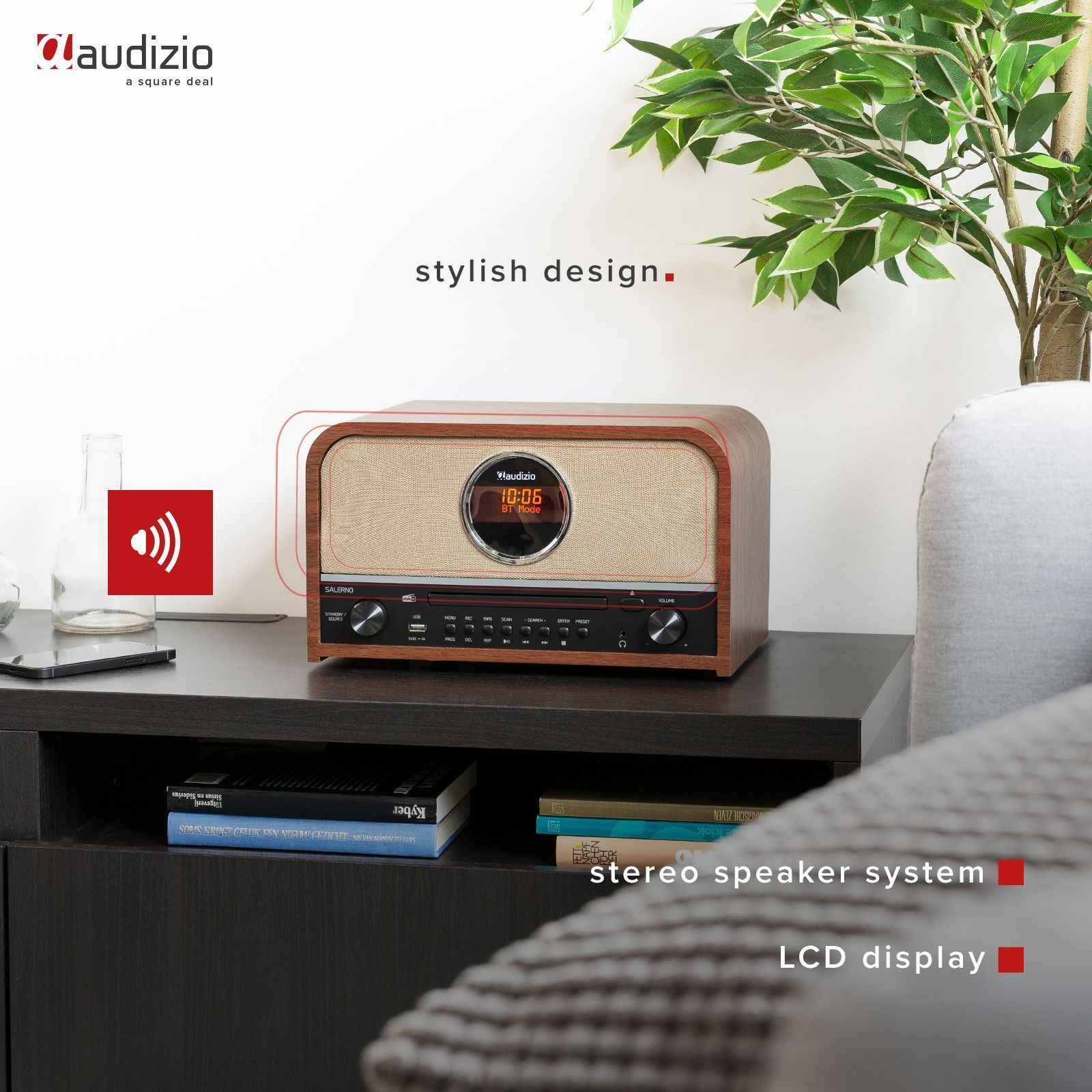 Holzradio auf einem Tisch mit Pflanze und Buch. Das Radio zeigt die Uhrzeit an.