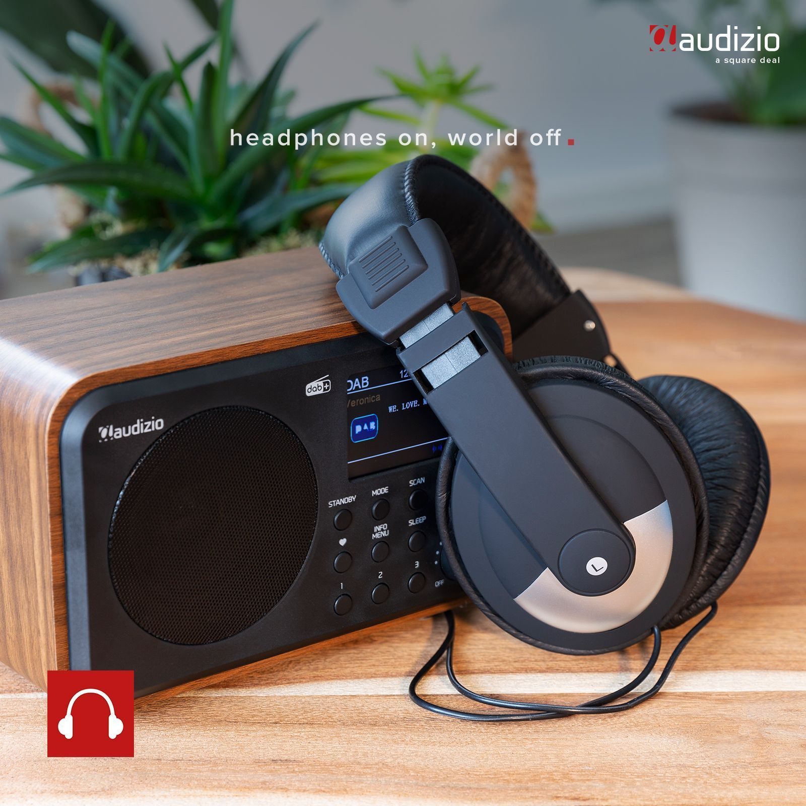 Schwarze Kopfhörer auf einem Holzradio mit einer Pflanze. Der Text lautet 'Kopfhörer an, Welt aus'.