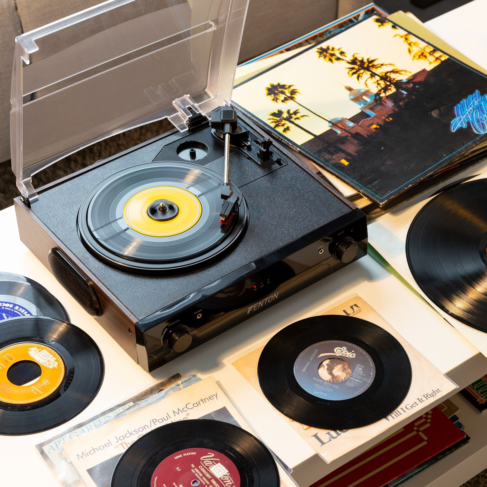 Plattenspieler mit Schallplatten und Albumcovern auf weißer Oberfläche. Markenname Fenton sichtbar.