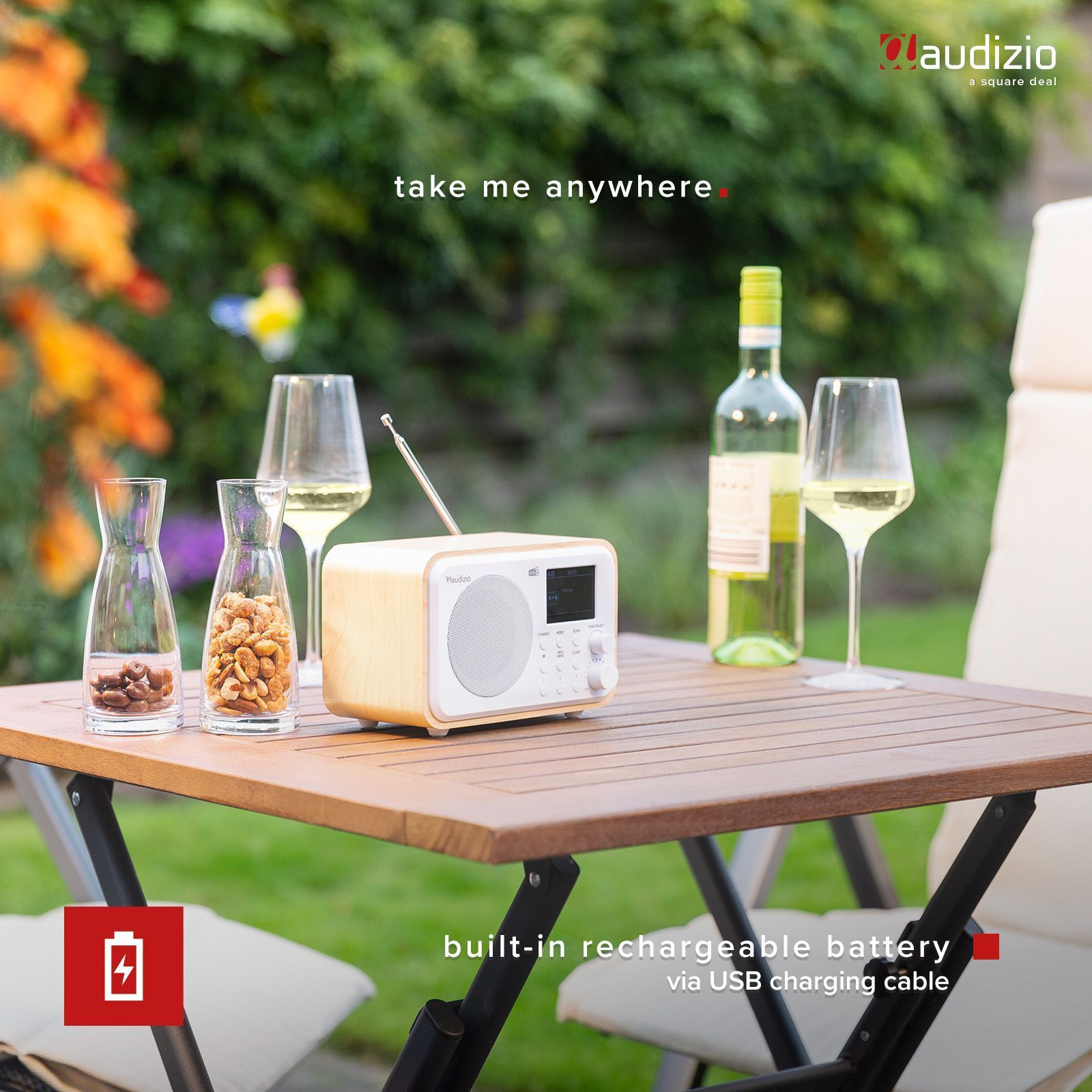 Radio en una mesa de madera. Dos copas, botella de vino y aperitivos. Entorno al aire libre.