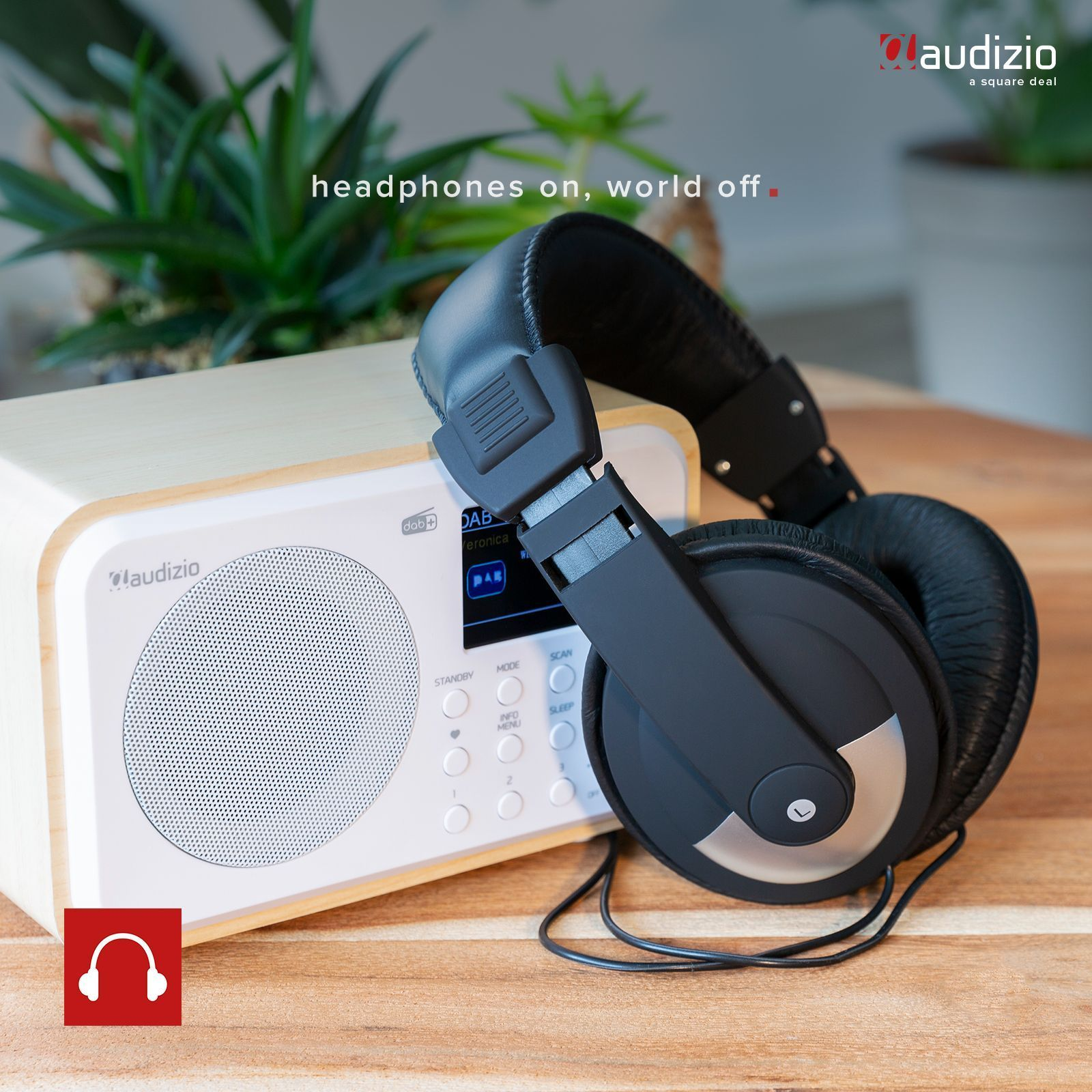 Una radio con auriculares. La escena muestra auriculares sobre una mesa de madera con plantas verdes en el fondo.