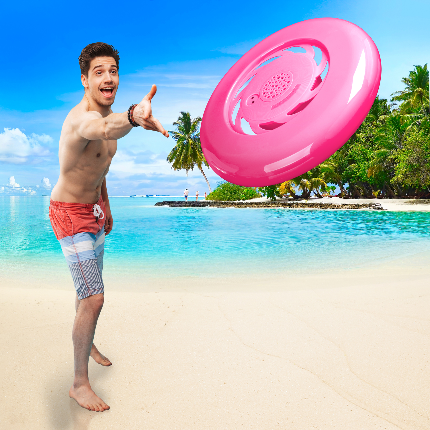 Een man in zwembroek gooit een roze frisbee op een strand met een blauwe lucht en palmbomen op de achtergrond.