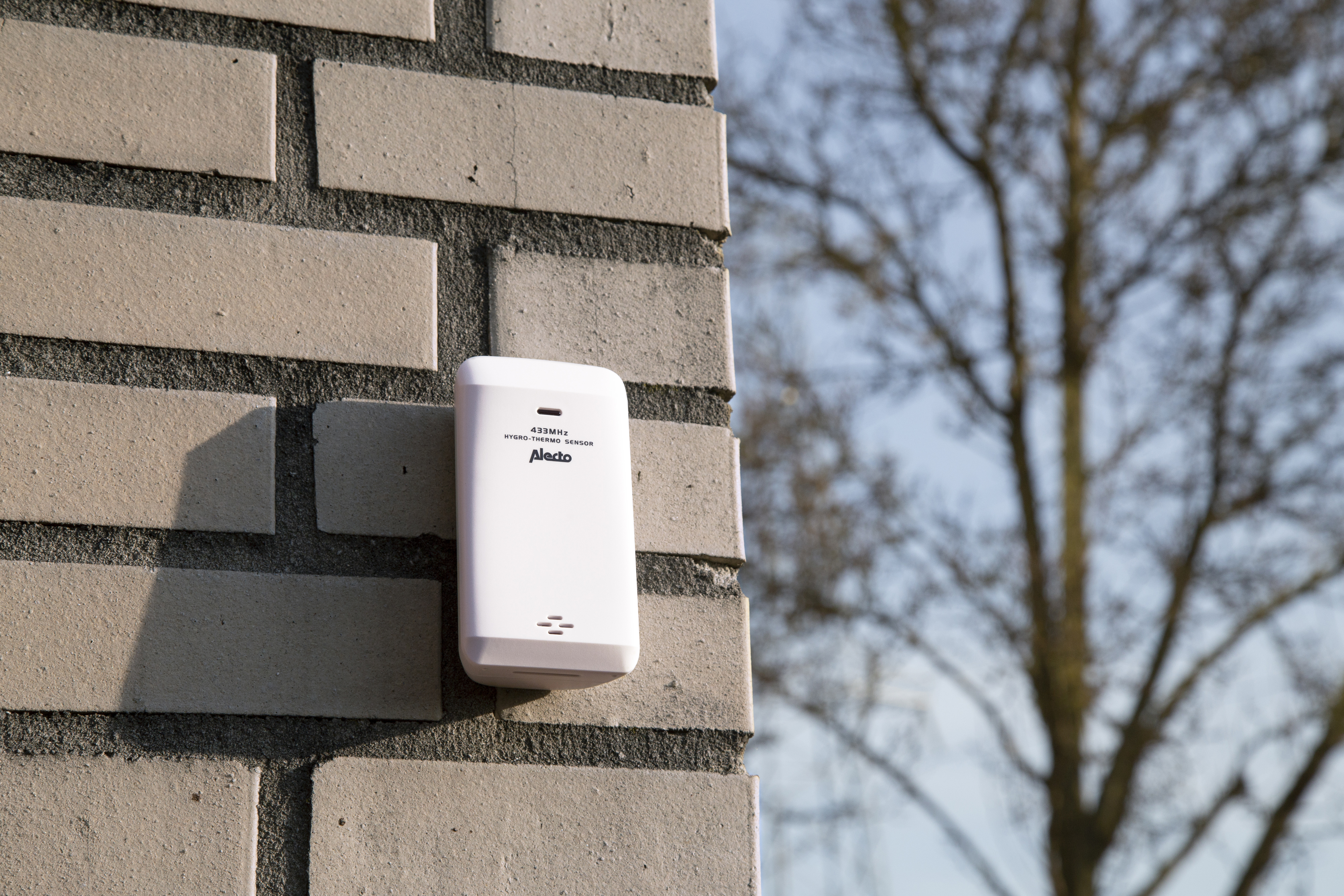 Witte beveiligingssensor gemonteerd op een bakstenen muur.