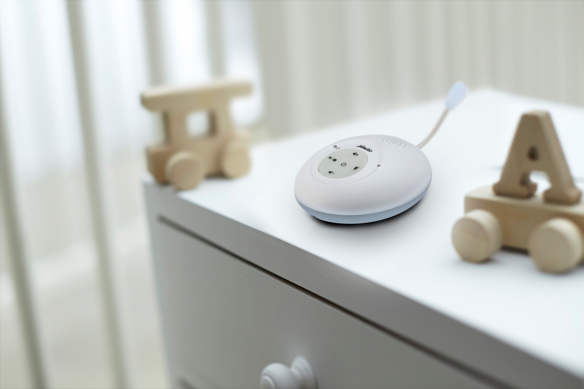 Baby monitor on a white surface, wooden toy train and letter A on the sides, soft background.