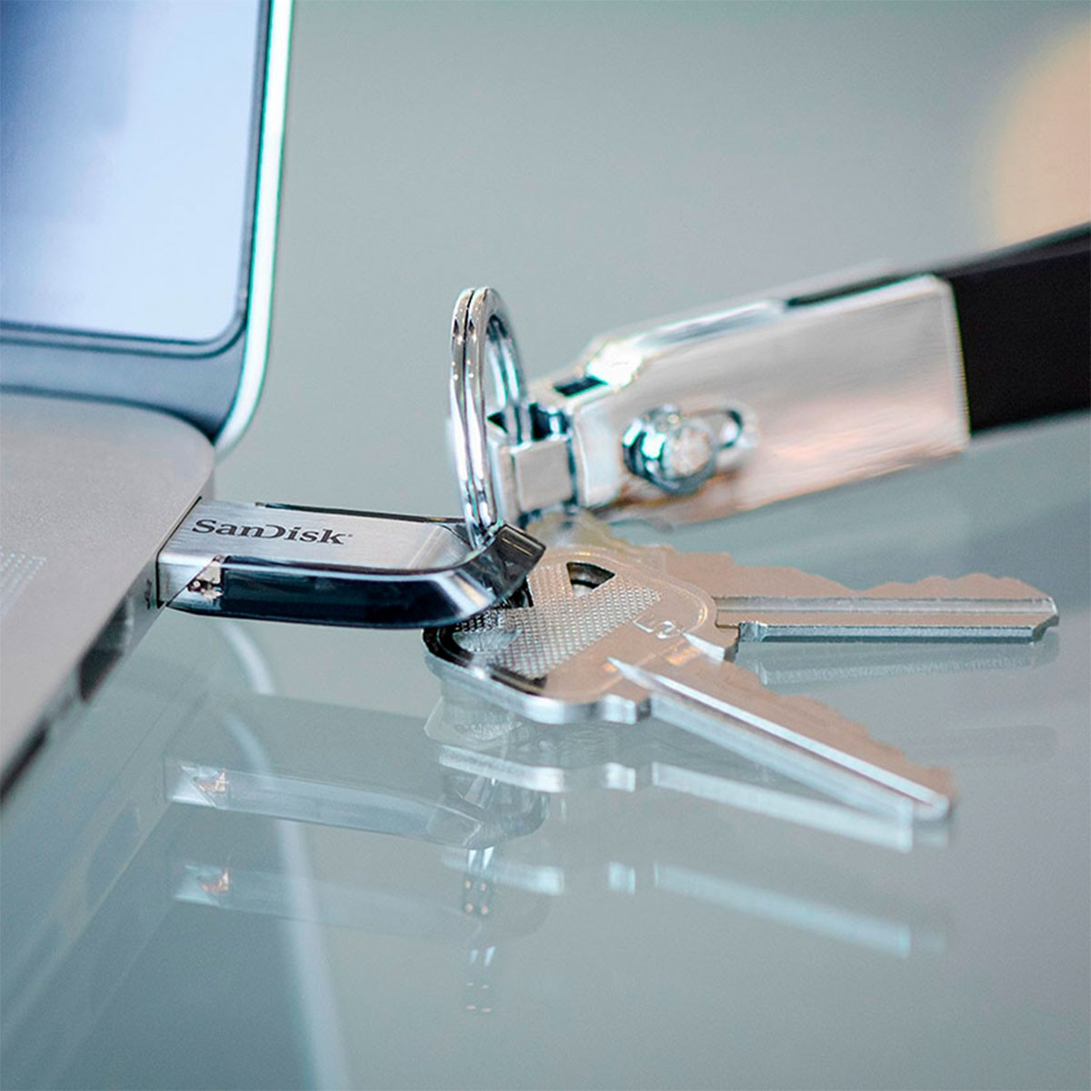 Pendrive i klucze obok laptopa, zbliżenie na odblaskowej powierzchni.