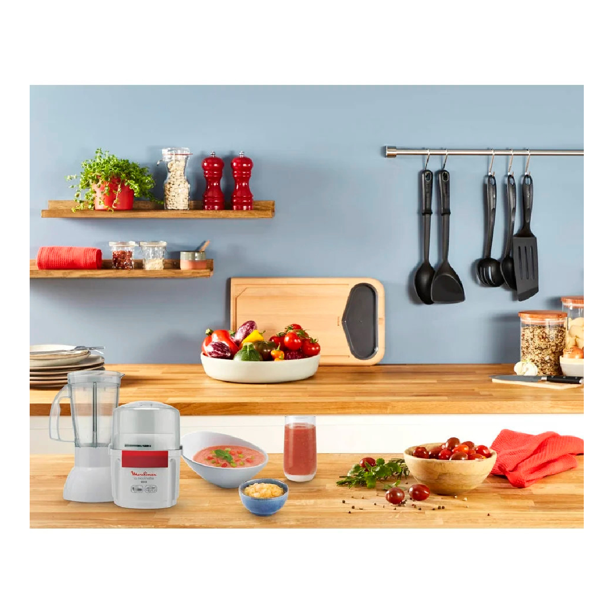 Una scena di cucina con vari ingredienti, utensili e un frullatore, contro un muro blu.