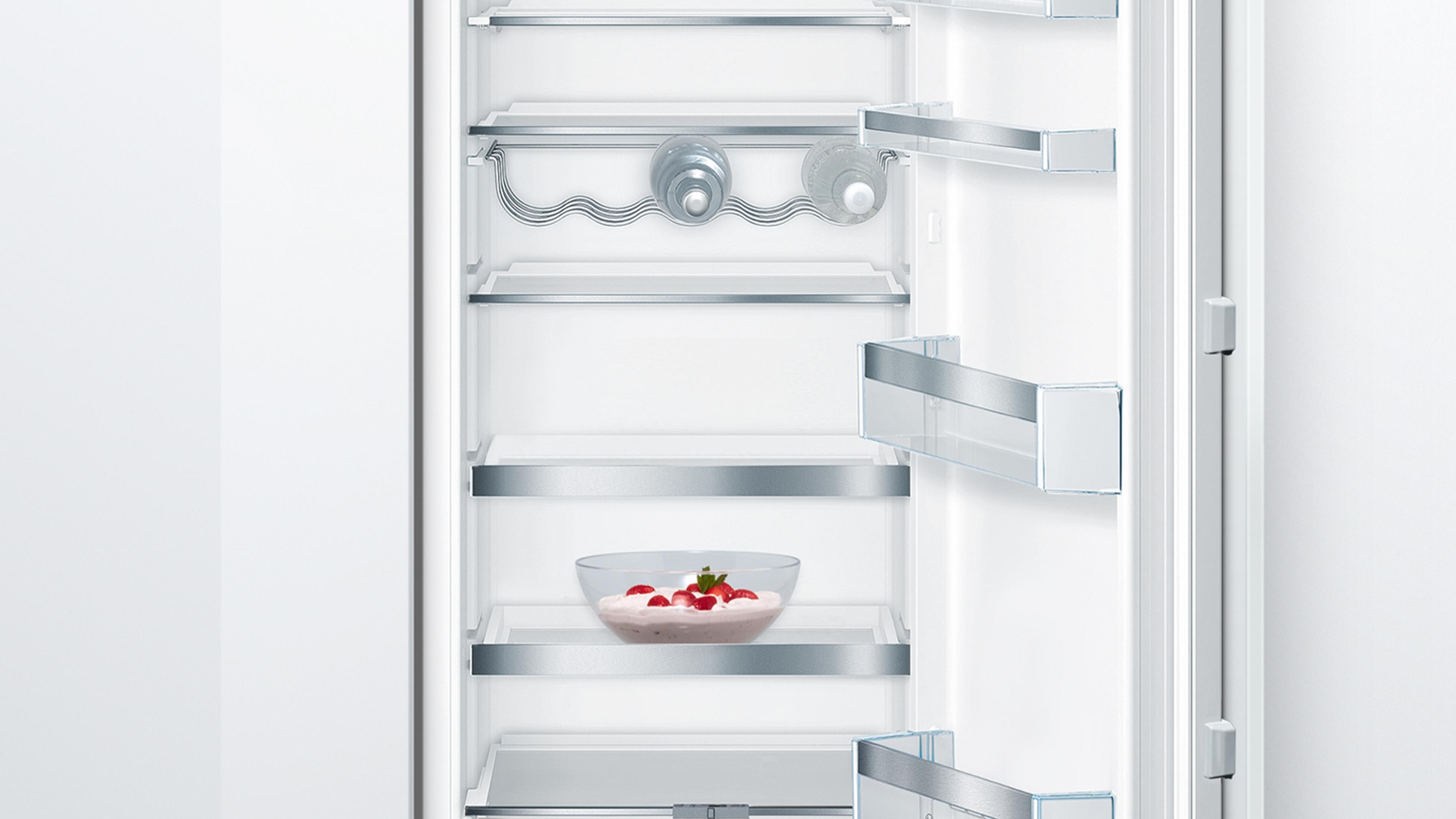 White refrigerator interior with glass shelves, bottle holders, and a bowl of dessert.
