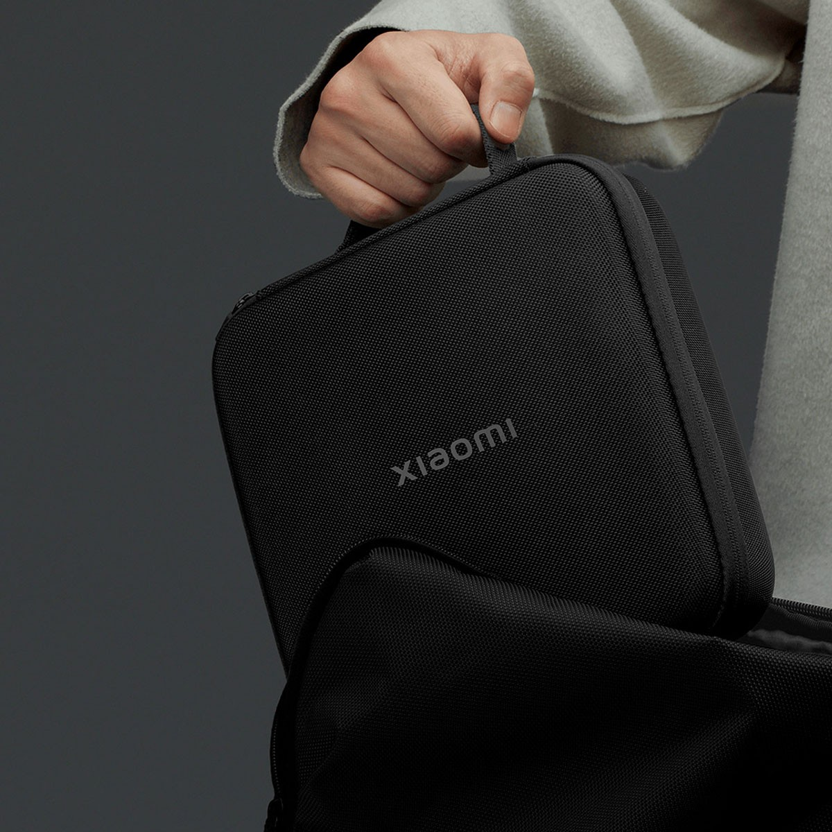 Persona che tiene una custodia nera con scritto "Xiaomi", vicino a uno zaino.