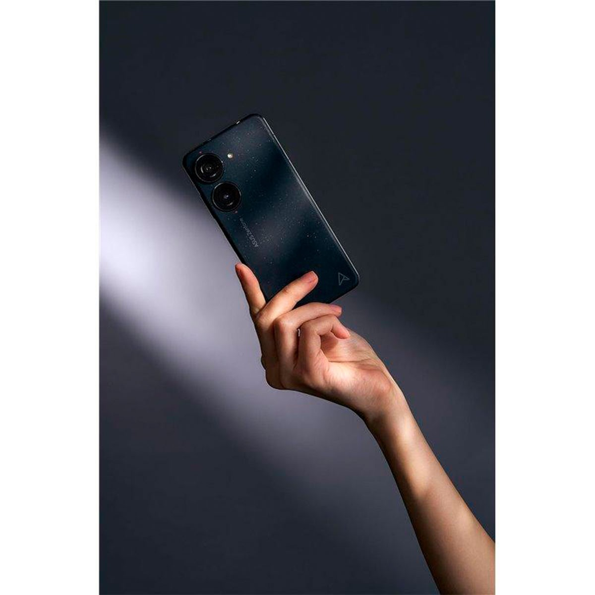 Mano che tiene un telefono scuro. Lo sfondo è grigio scuro. Obiettivi della fotocamera visibili.