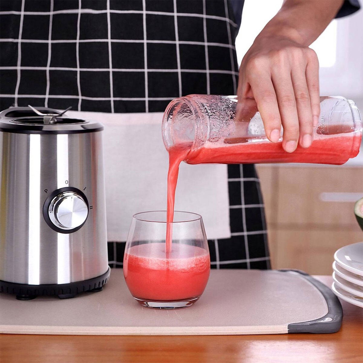 Person gießt rote Flüssigkeit aus einem Glas in ein Glas, neben einem Mixer.