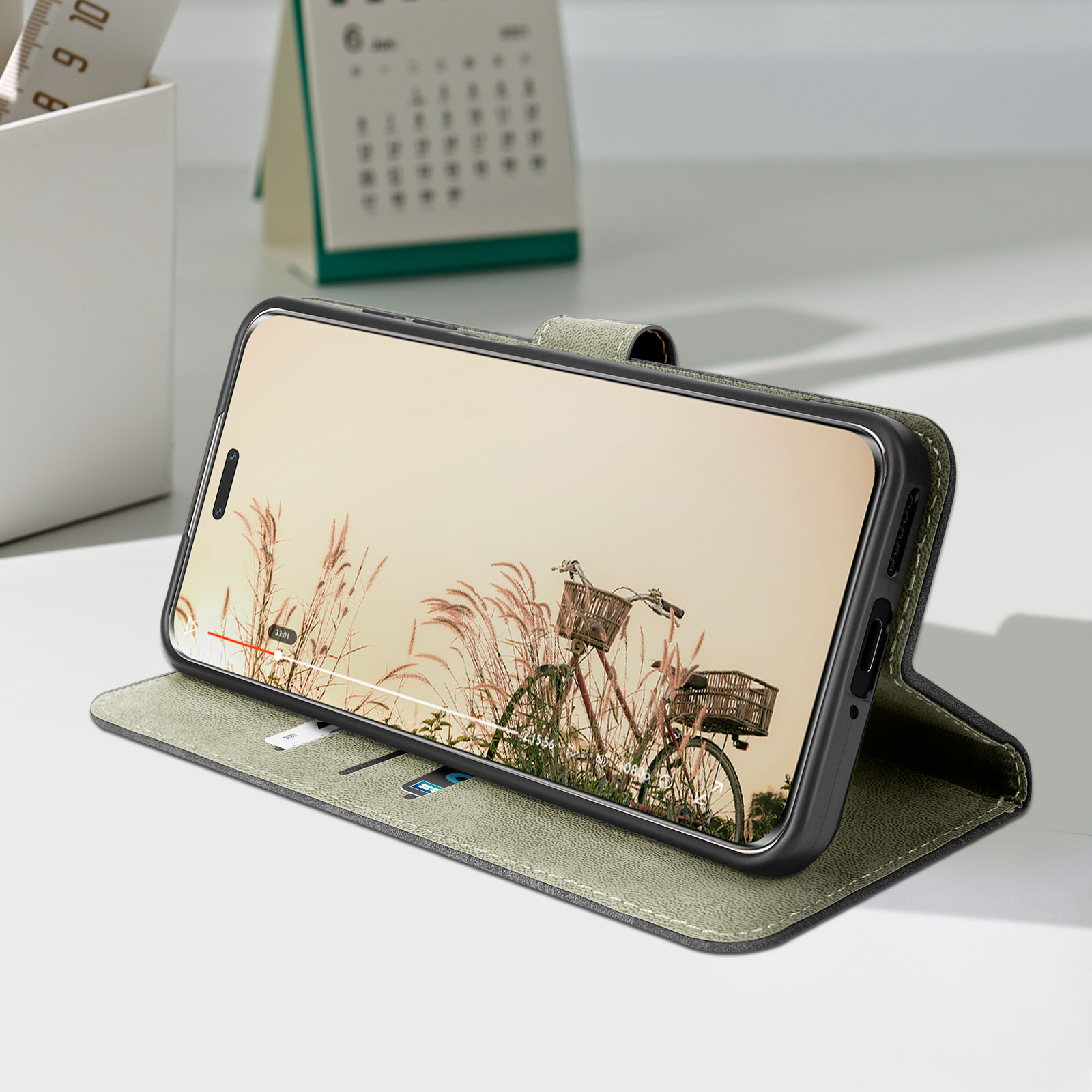 Téléphone affichant une scène de vélo dans un étui. Calendrier et porte-stylo sur la table.