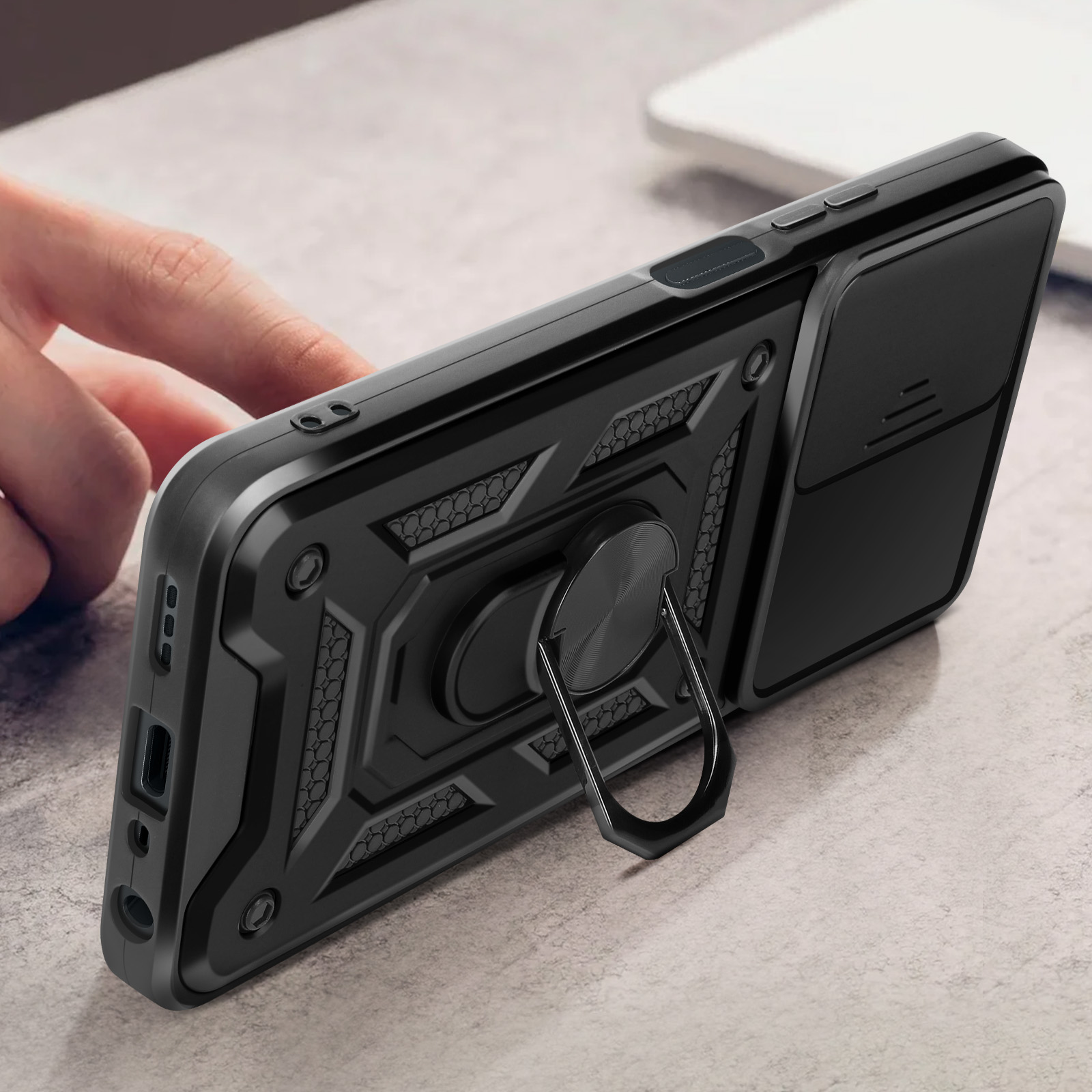 Custodia nera per telefono con supporto ad anello. Una mano tiene il telefono. C'è una copertura sulla fotocamera.