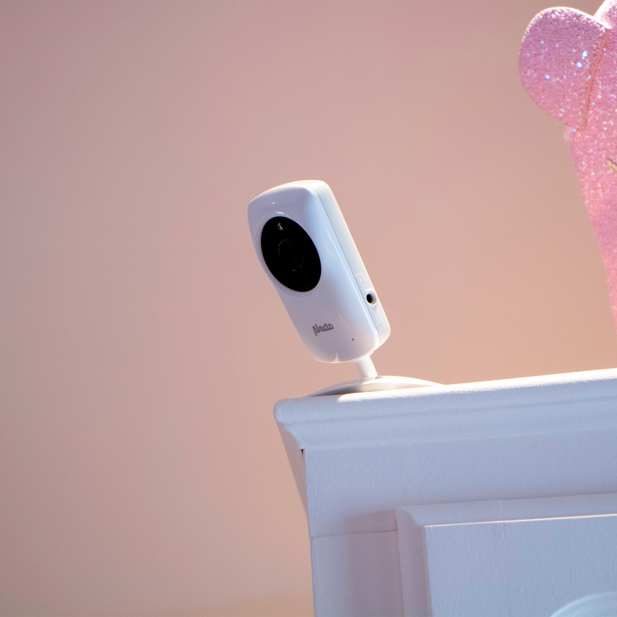 Witte babyfooncamera op een wit oppervlak met een roze achtergrond en een roze decoratie.