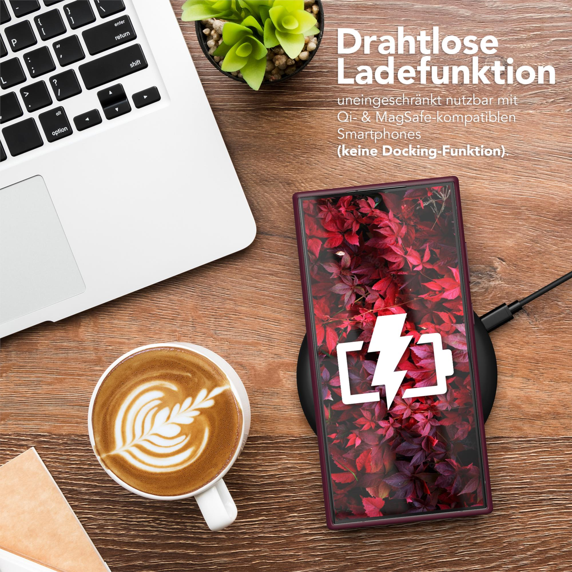 Ein Laptop, eine Tasse Kaffee mit Kunst und ein Telefon, das auf einem kabellosen Ladegerät lädt, auf einem Holztisch.
