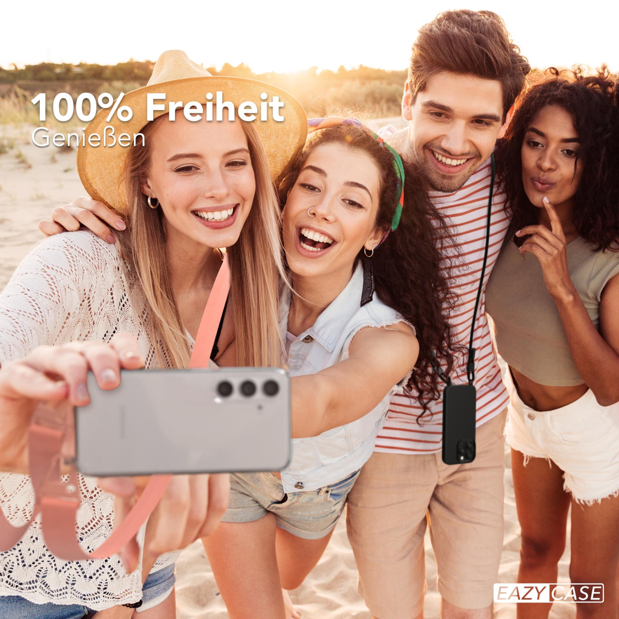 Vier Personen machen ein Selfie am Strand. Einer hält Telefon mit Gurt. Fröhliche Ausdrücke.