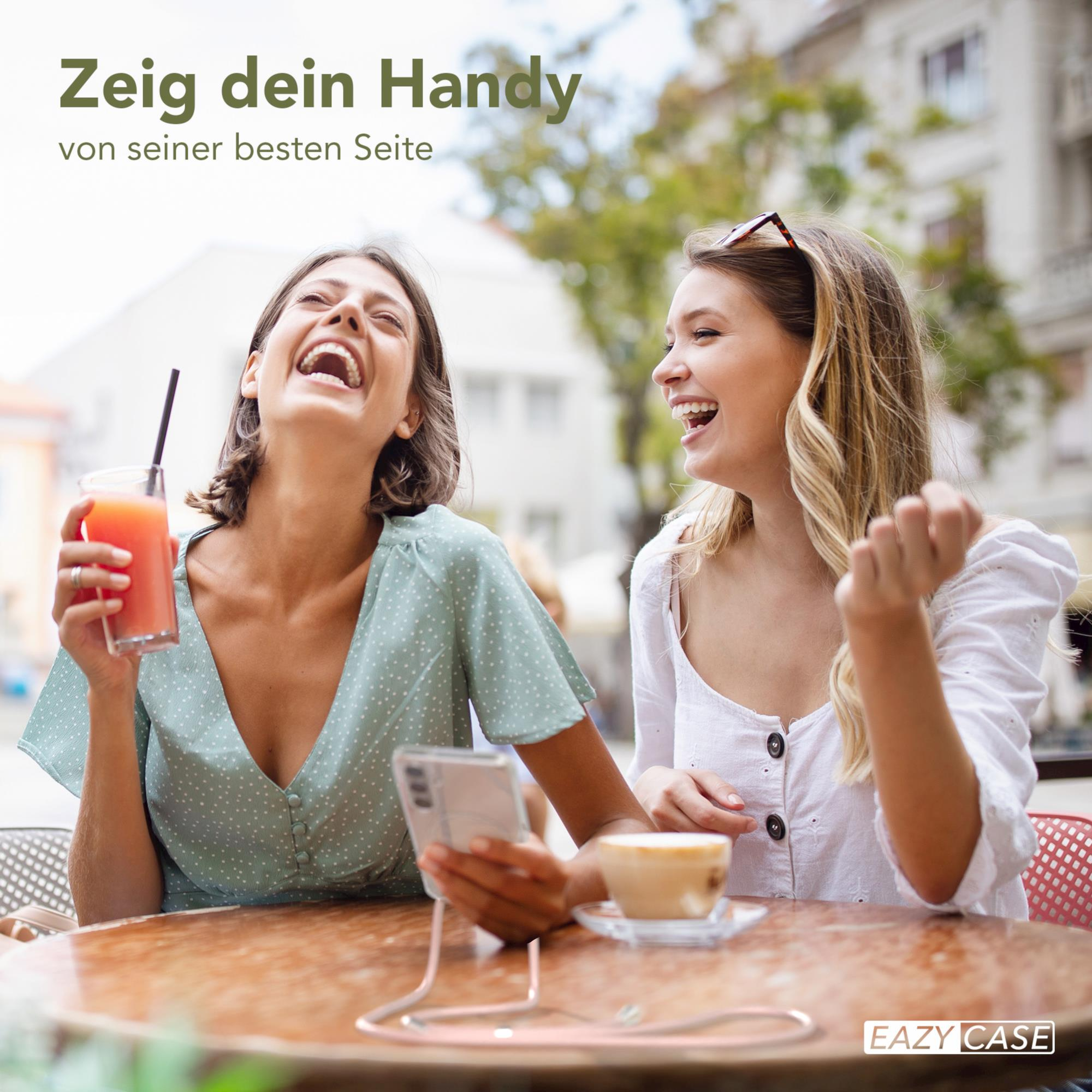 Zwei lachende Frauen, die Telefone halten, in einem Café im Freien.