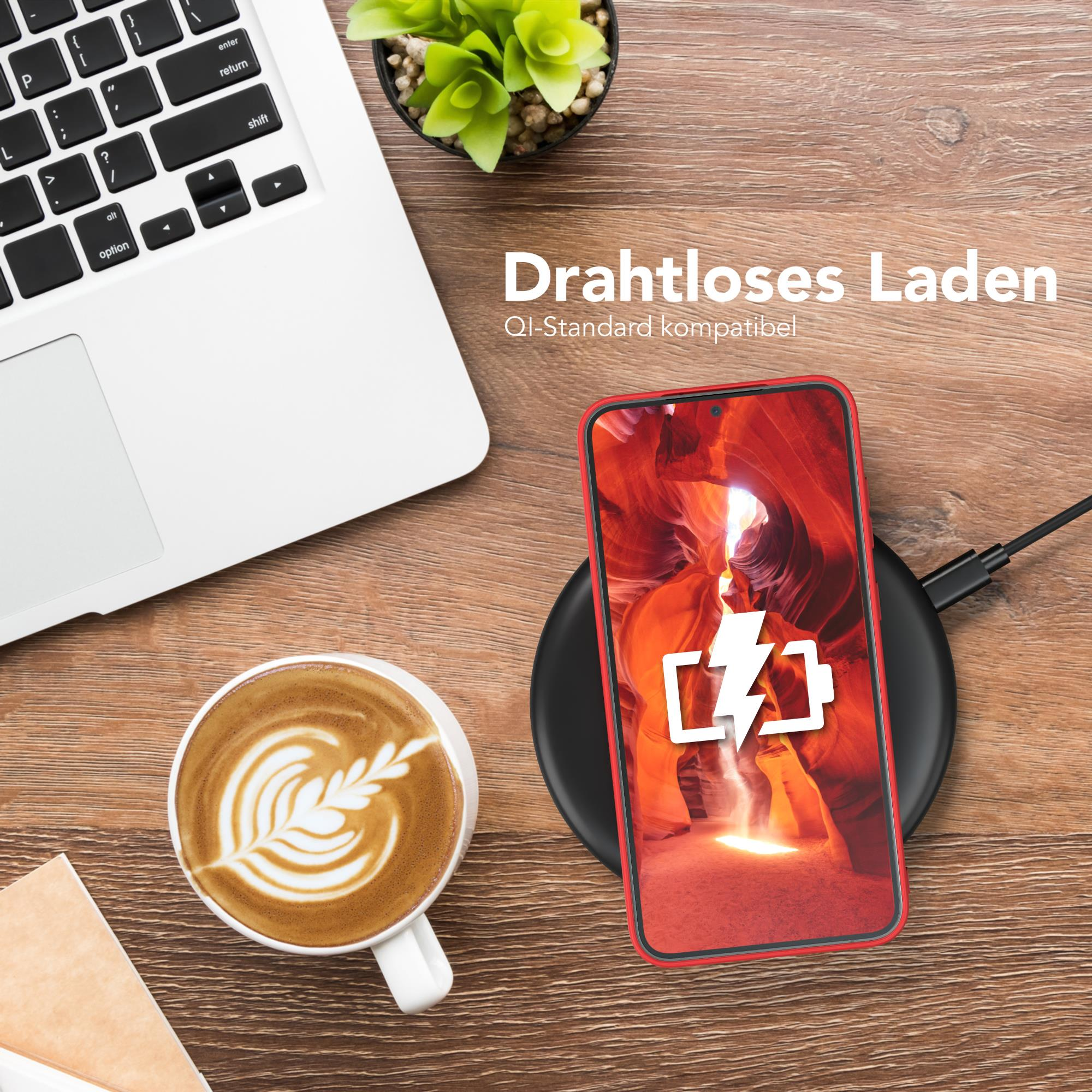 Telefon wird drahtlos auf einem schwarzen Pad geladen. Ein Laptop, eine Kaffeetasse und eine Pflanze im Hintergrund.