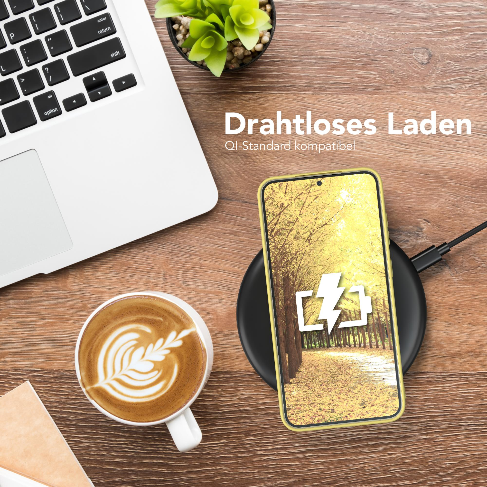 Telefon auf kabellosem Ladegerät, neben Laptop und Kaffeetasse, auf Holztisch.
