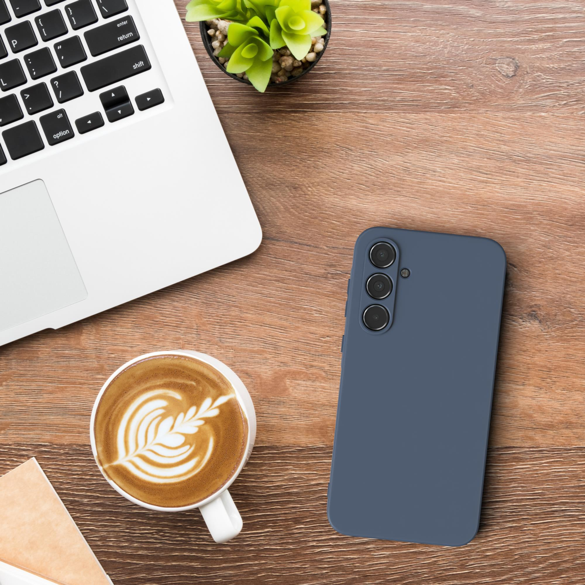 Ein blaues Telefon liegt neben einem Laptop und einer Tasse Kaffee mit Latte Art auf einem Holztisch.
