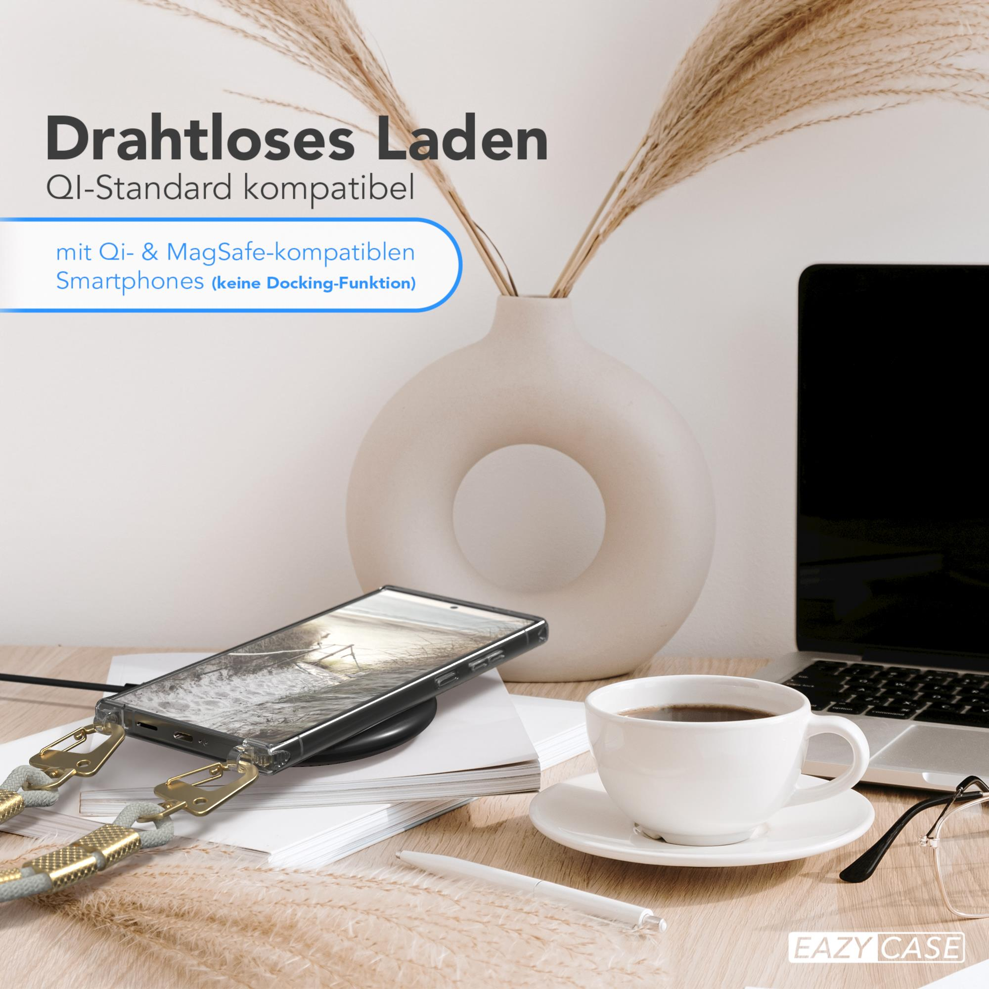 Ein Telefon, das auf einem schwarzen Pad geladen wird, neben einer Kaffeetasse, einer Vase mit Pflanzen und einem Laptop.