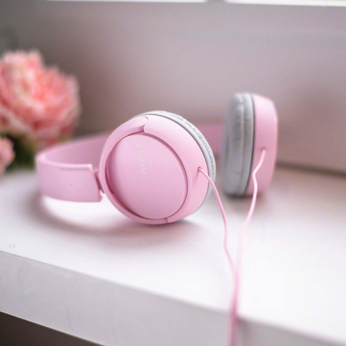 Casque rose posé sur une surface blanche, avec un arrière-plan floral flou.