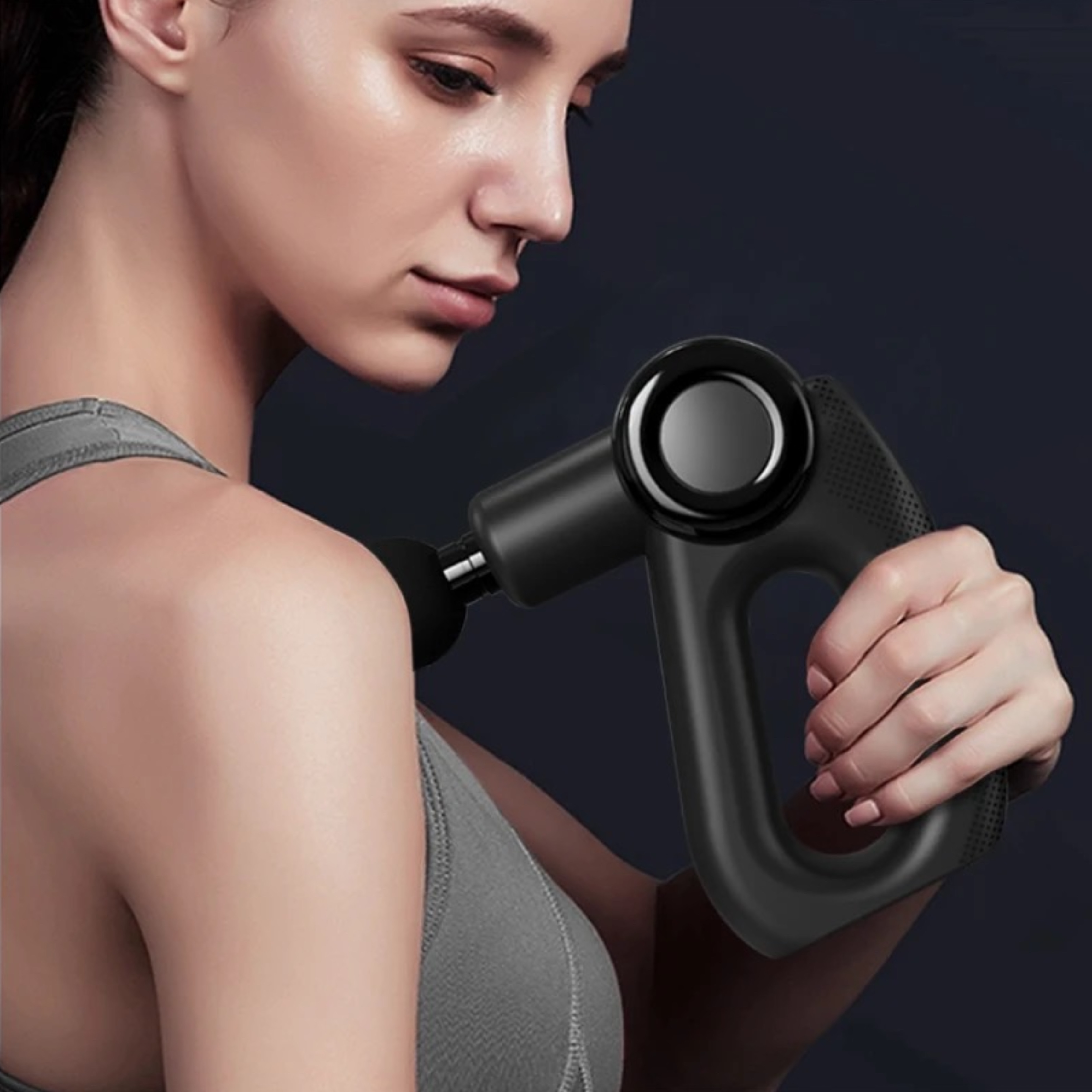 Kobieta używa czarnego pistoletu do masażu na ramieniu. Ma na sobie szarą górę.