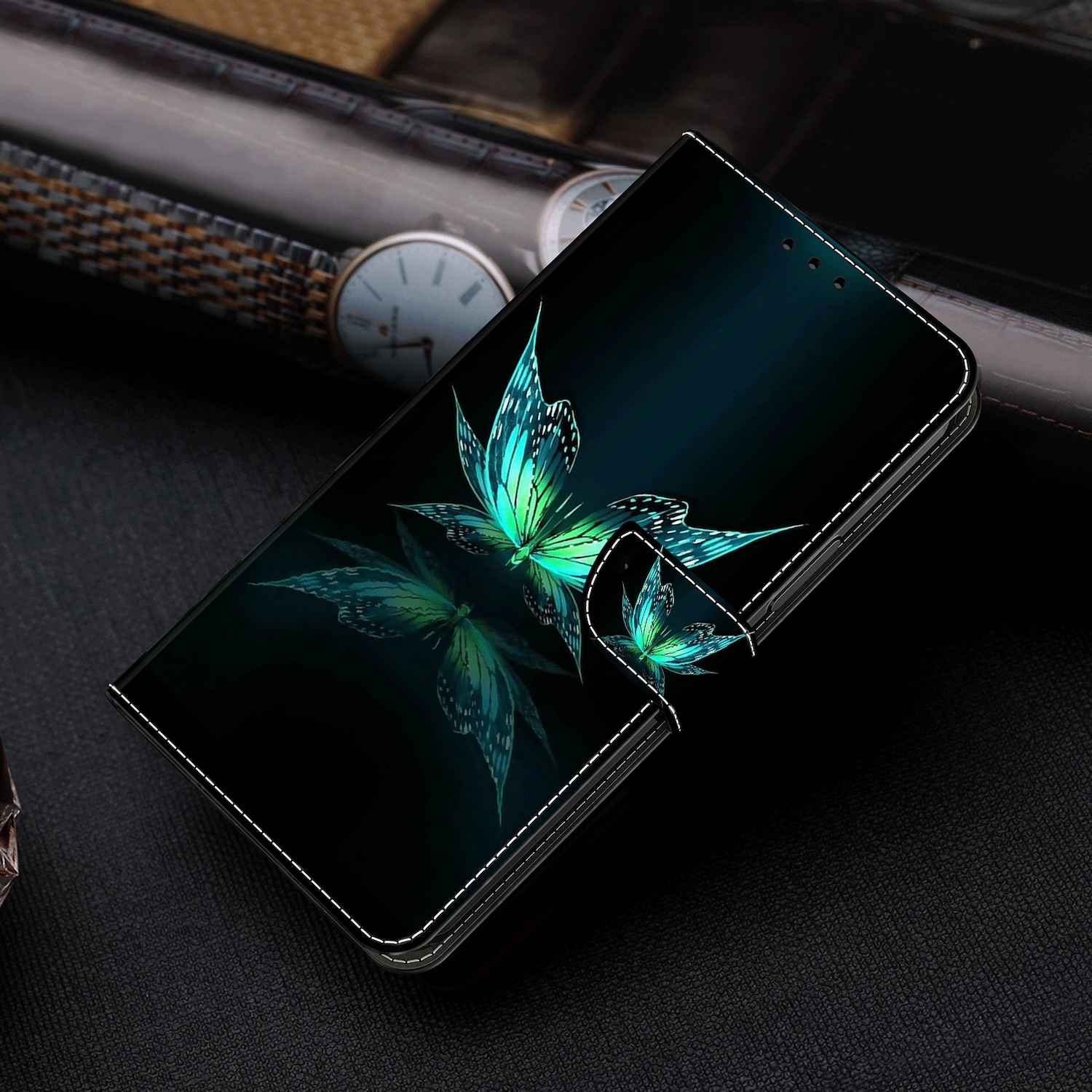 Schwarze Handyhülle mit Schmetterlingsdesign. Auf schwarzer Oberfläche mit Uhr.