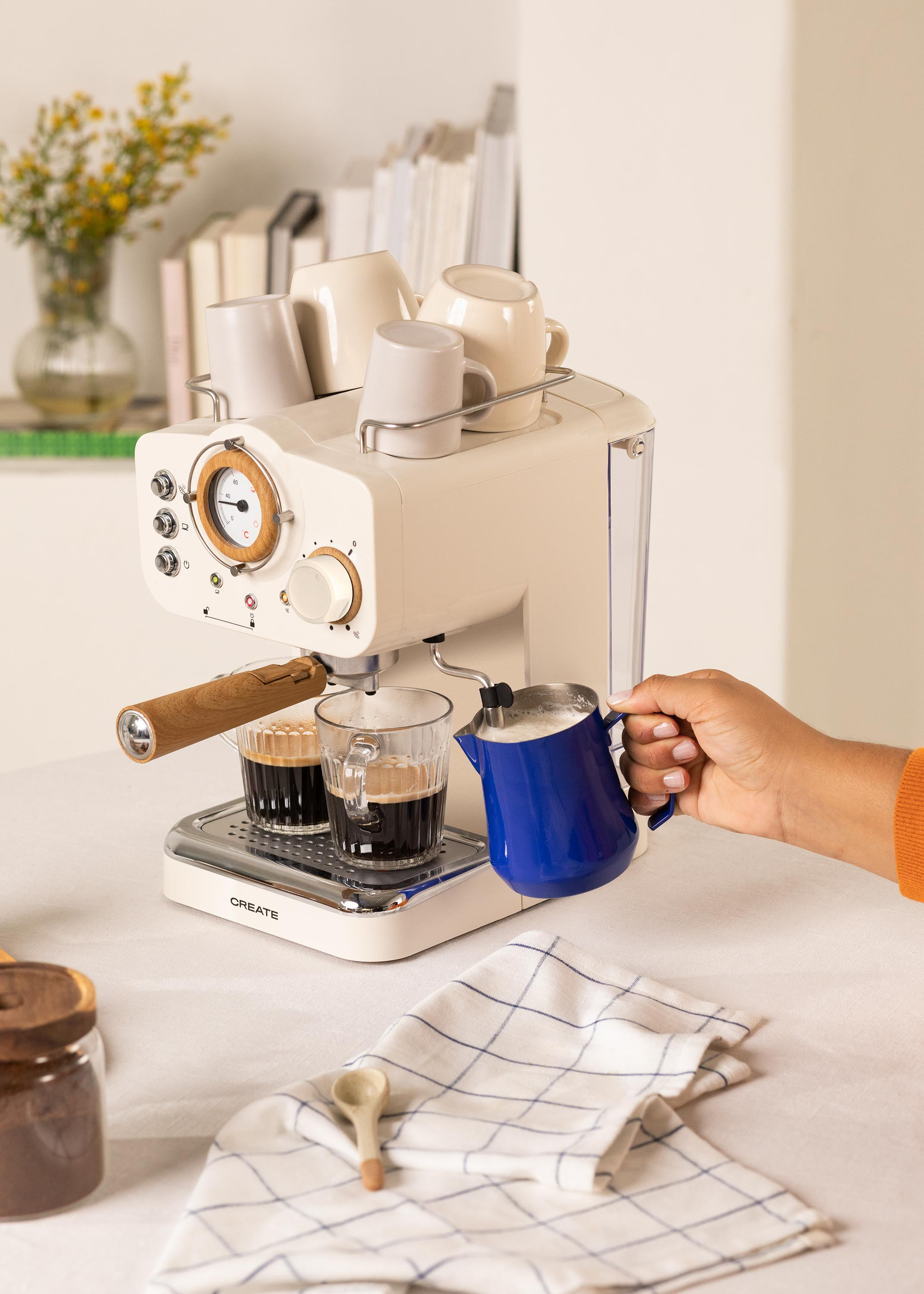 Máquina de café con tazas, una taza de café que se llena y una persona vertiendo leche. Crema y café.