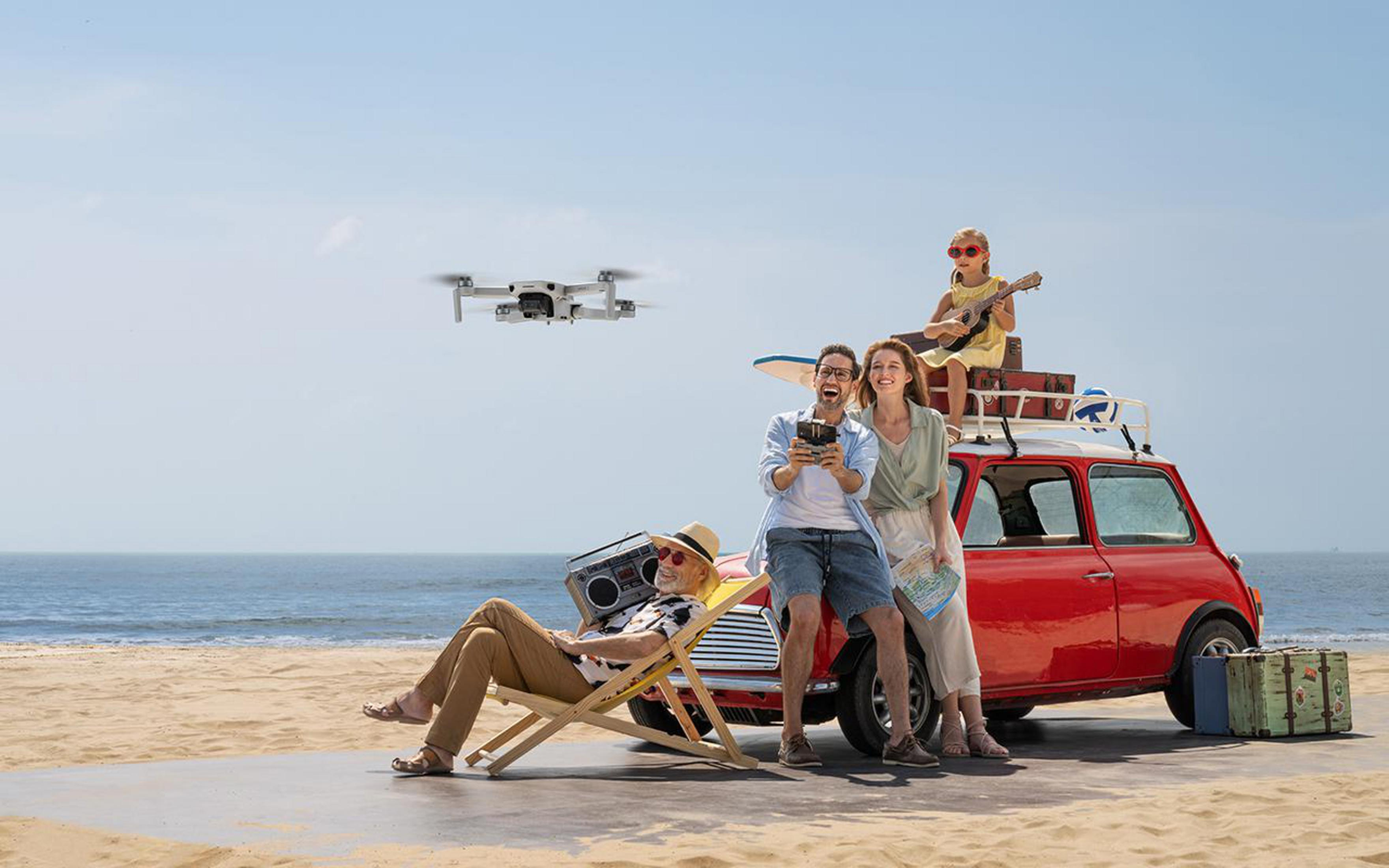 Familie am Strand mit fliegender Drohne. Rotes Auto. Fröhliche Leute, sonniger Tag.