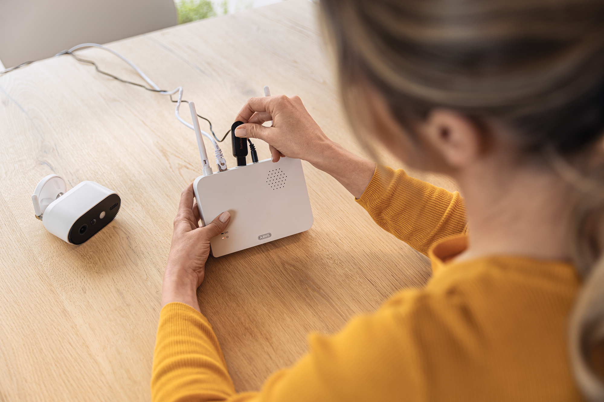 Una persona collega i cavi a un router bianco. Una telecamera di sicurezza è sullo sfondo.