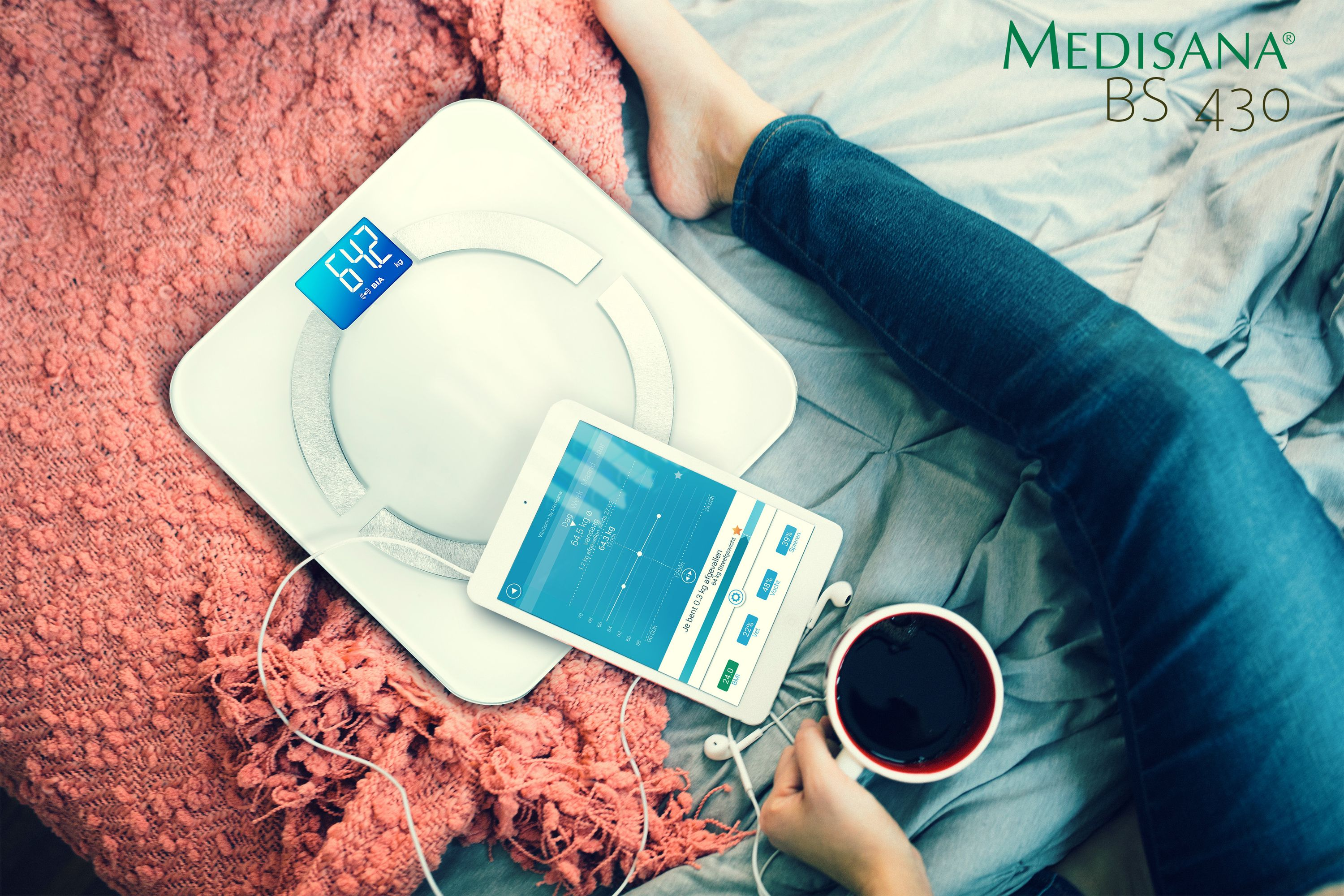 Osoba korzystająca z wagi i tabletu. Obecny kubek z kawą i telefon.