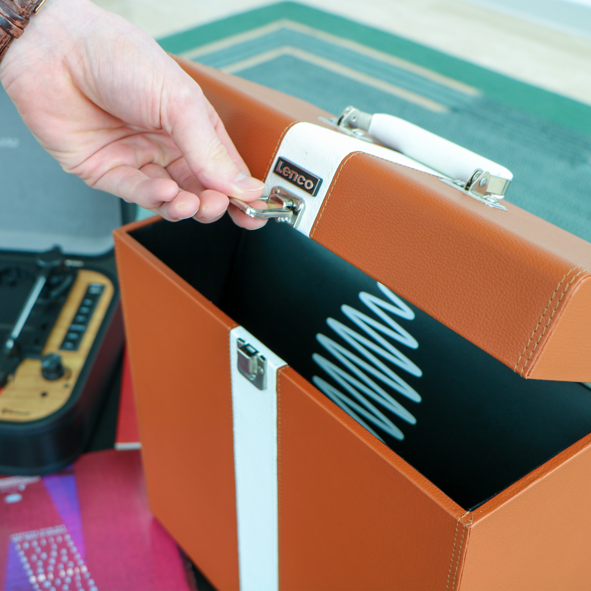 Ręka osoby otwierającej brązowo-biały futerał na płyty Lenco obok gramofonu.