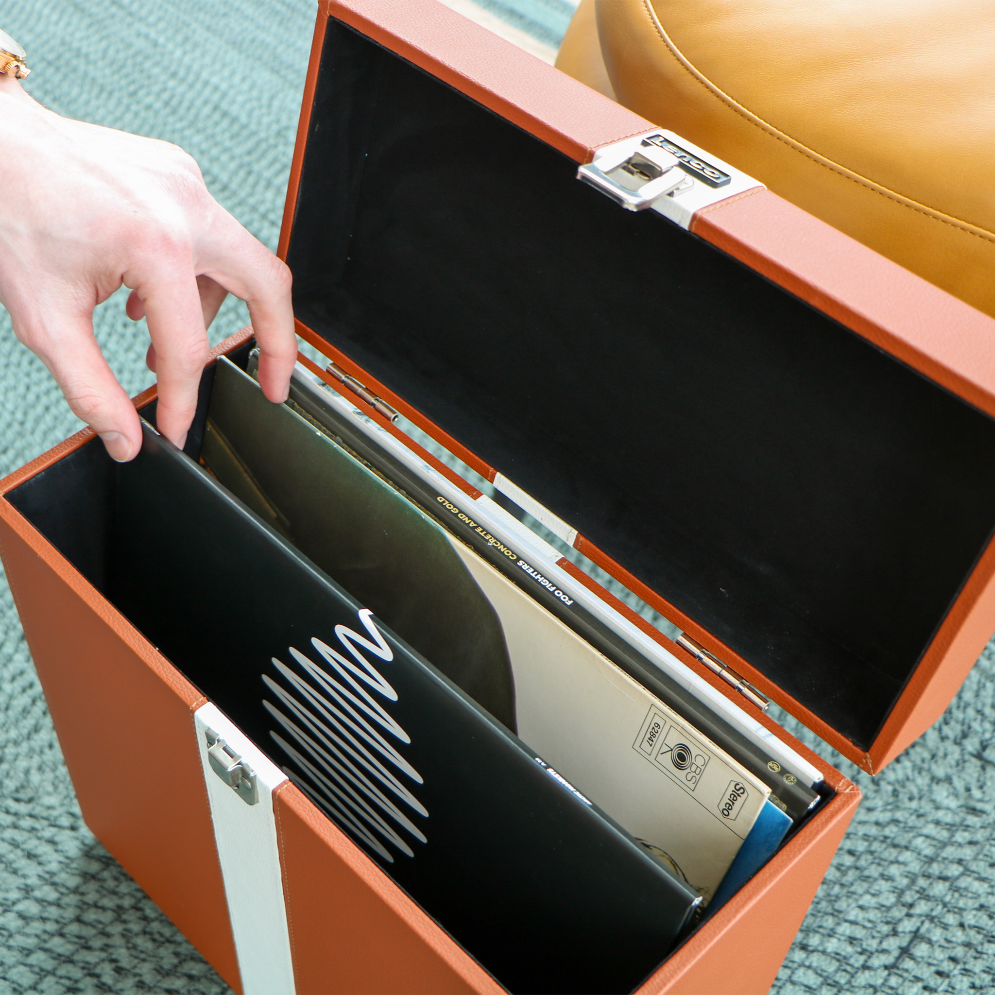 Ręka sięgająca do brązowego etui na płyty winylowe z płytami winylowymi w środku.