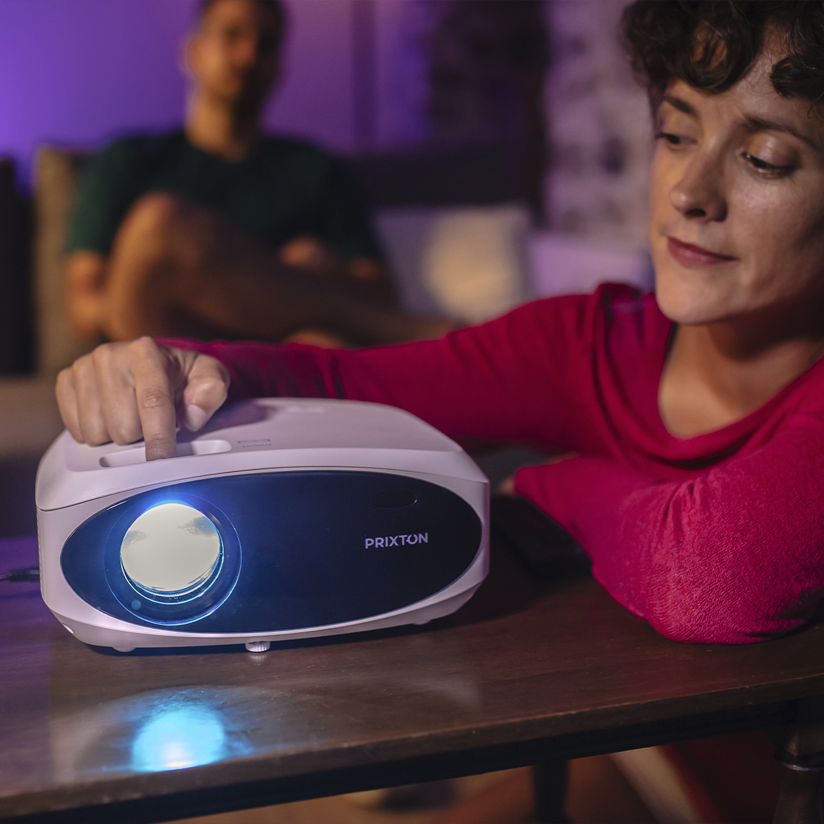 Kobieta obsługująca biały projektor na stole, druga osoba w tle.