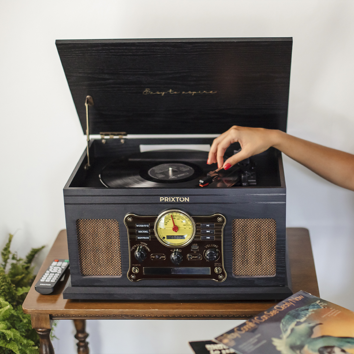 Gramofon w stylu vintage z ręką kobiety umieszczającą płytę na talerzu. Płyty i pilot widać.